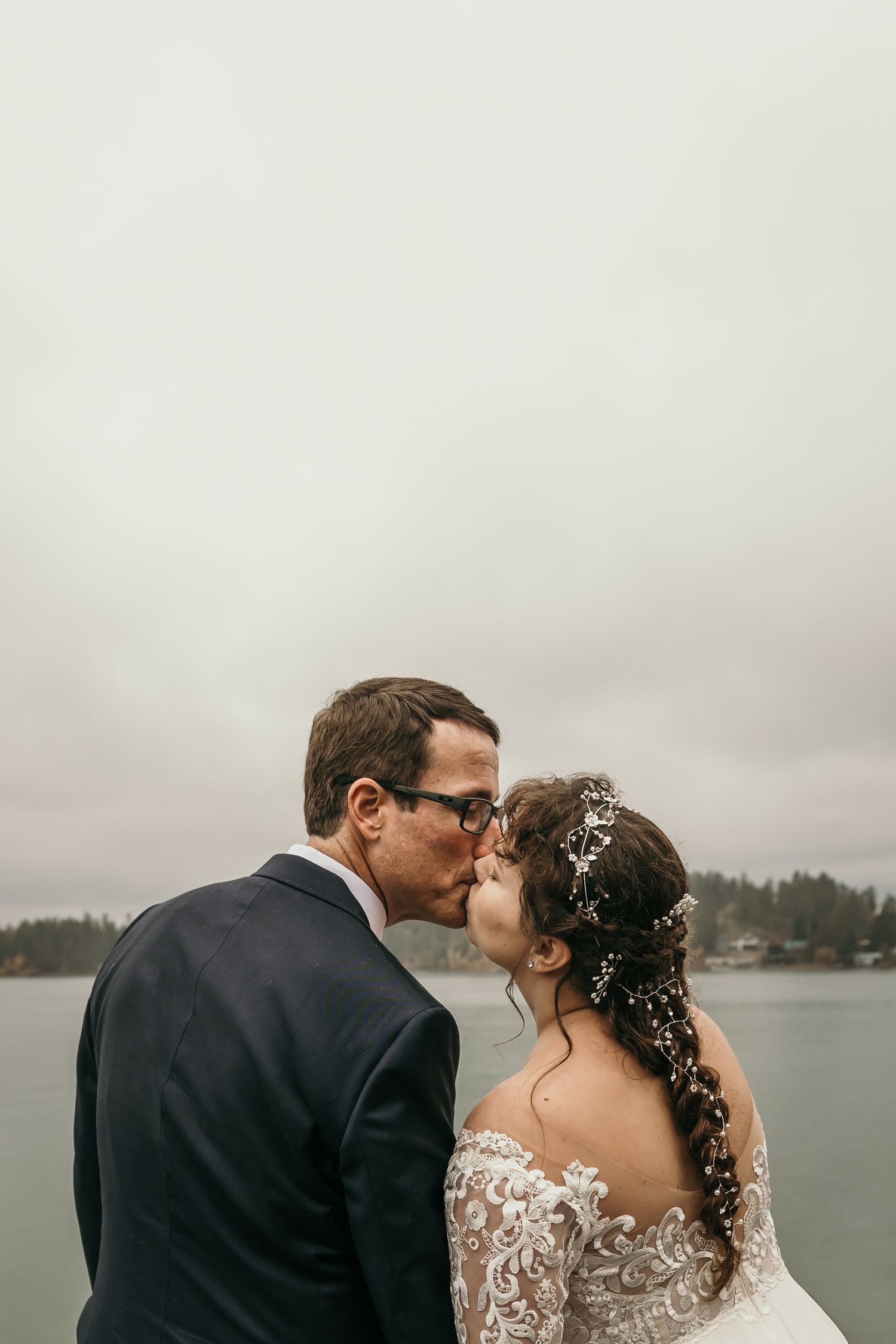 Bride and groom sharing a romantic kiss on a waterfront dock on their rainy wedding day.