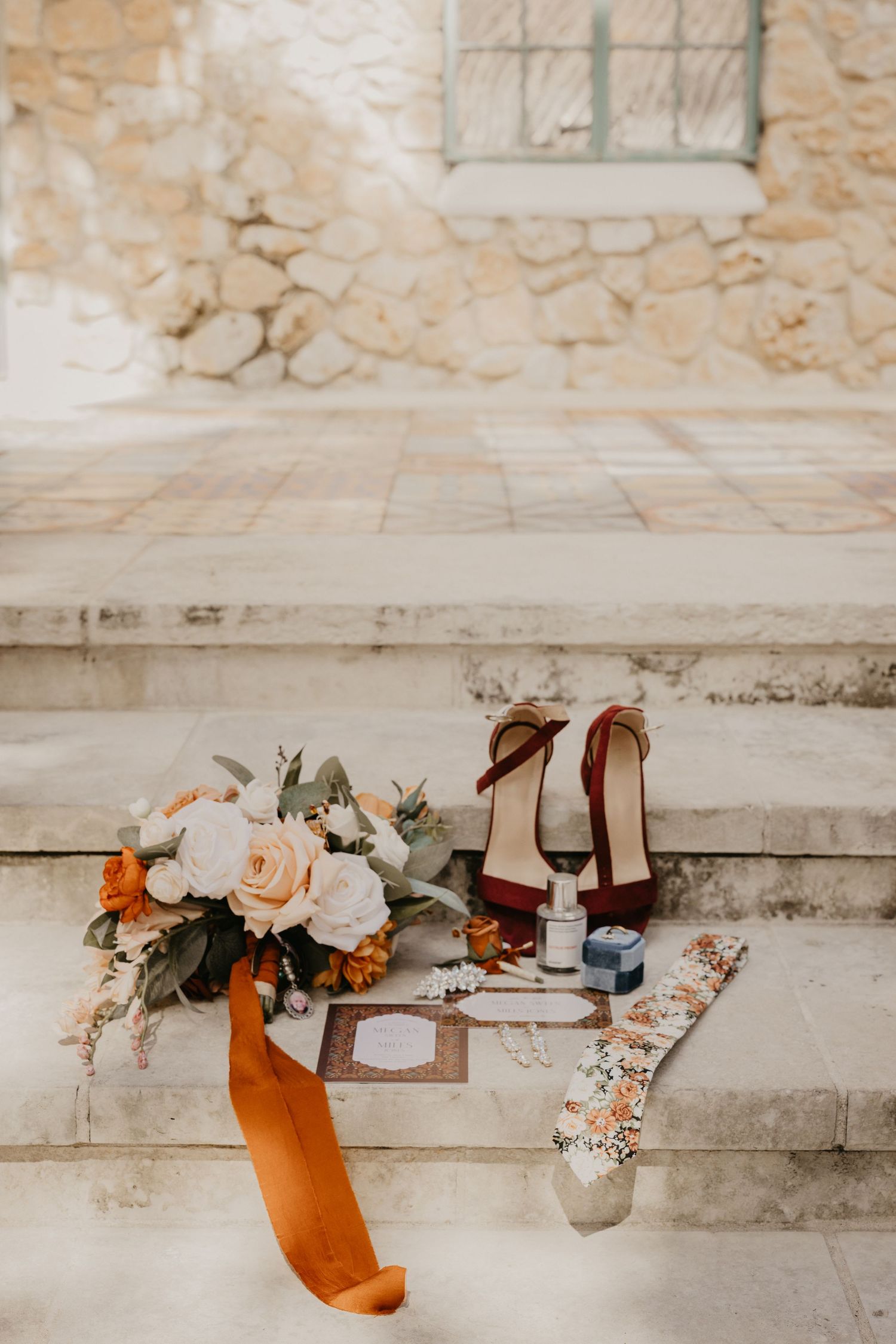 Wedding flat lay with bouquet, red heels, invitations, and accessories arranged on stone steps.