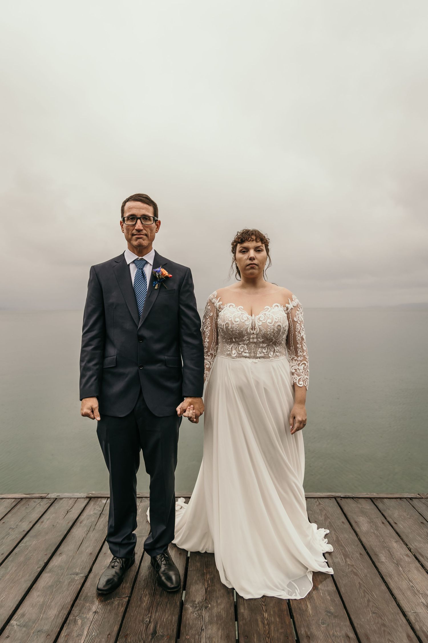 Bride and groom standing hand in hand on a foggy dock overlooking a calm lake on their wedding day.