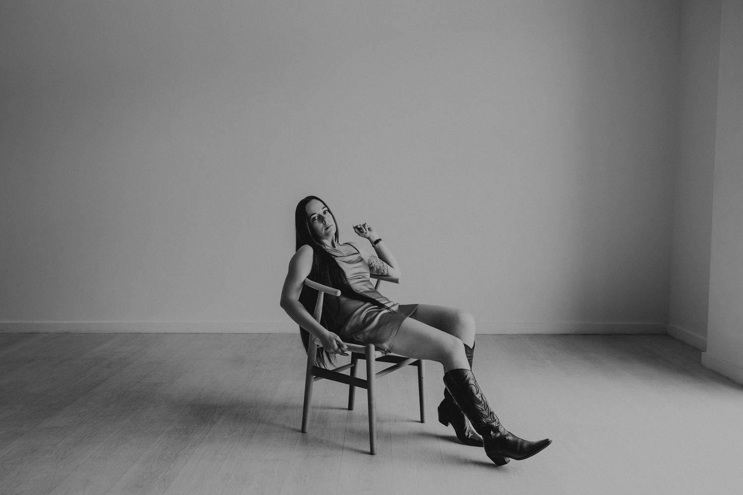 Black and white image of a woman in a dress and cowboy boots lounging on a wooden chair.