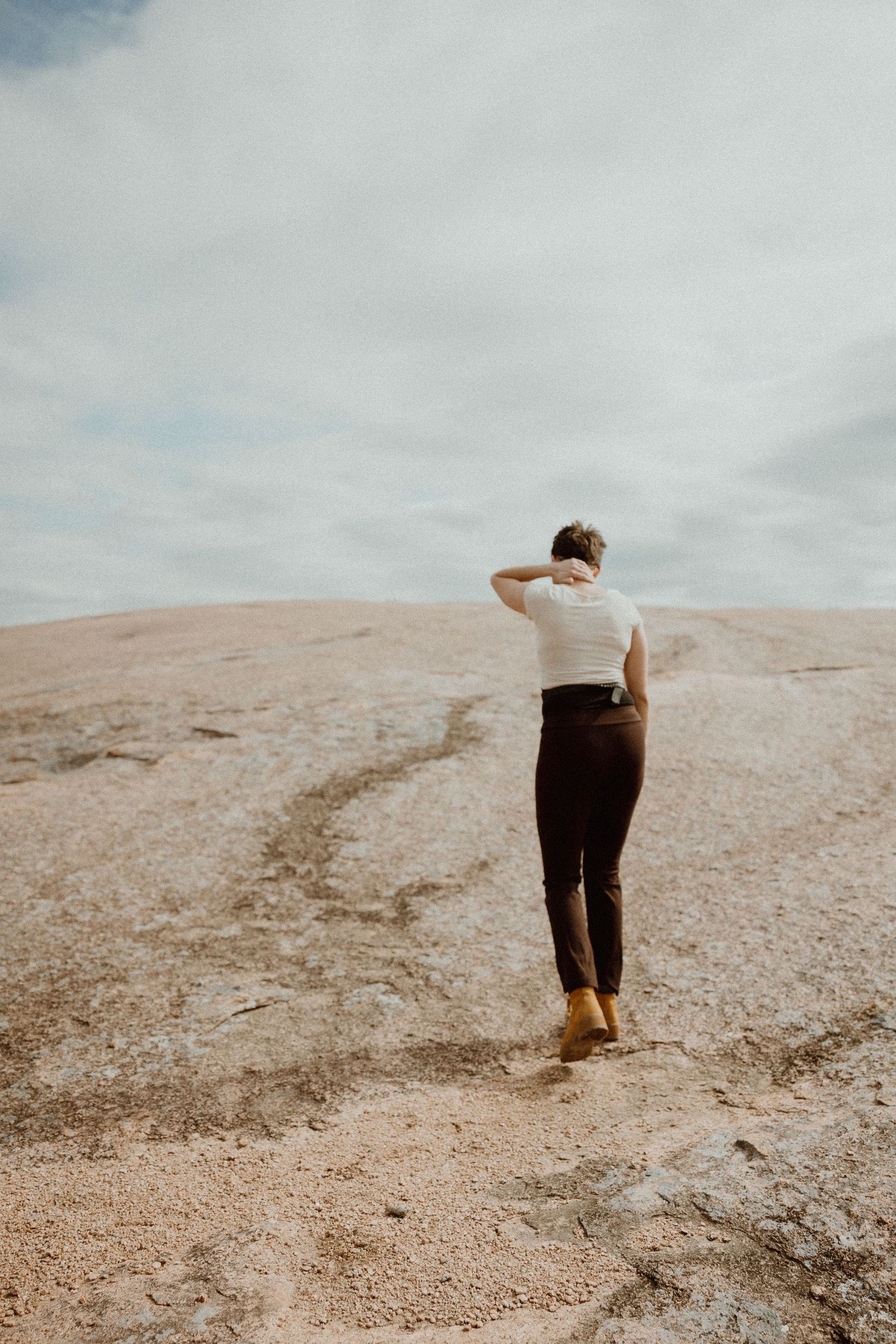 Person in white top and dark pants standing on vast rocky landscape under cloudy sky.