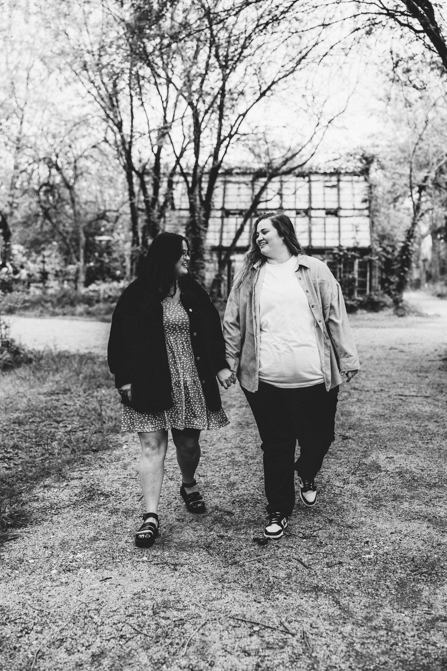 Black and white photo of two women holding hands and walking in a park.