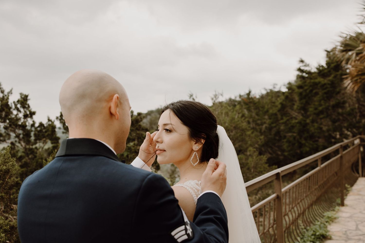 Groom gently wipes tears from brides cheek in an emotional outdoor wedding portrait on an overcast day.