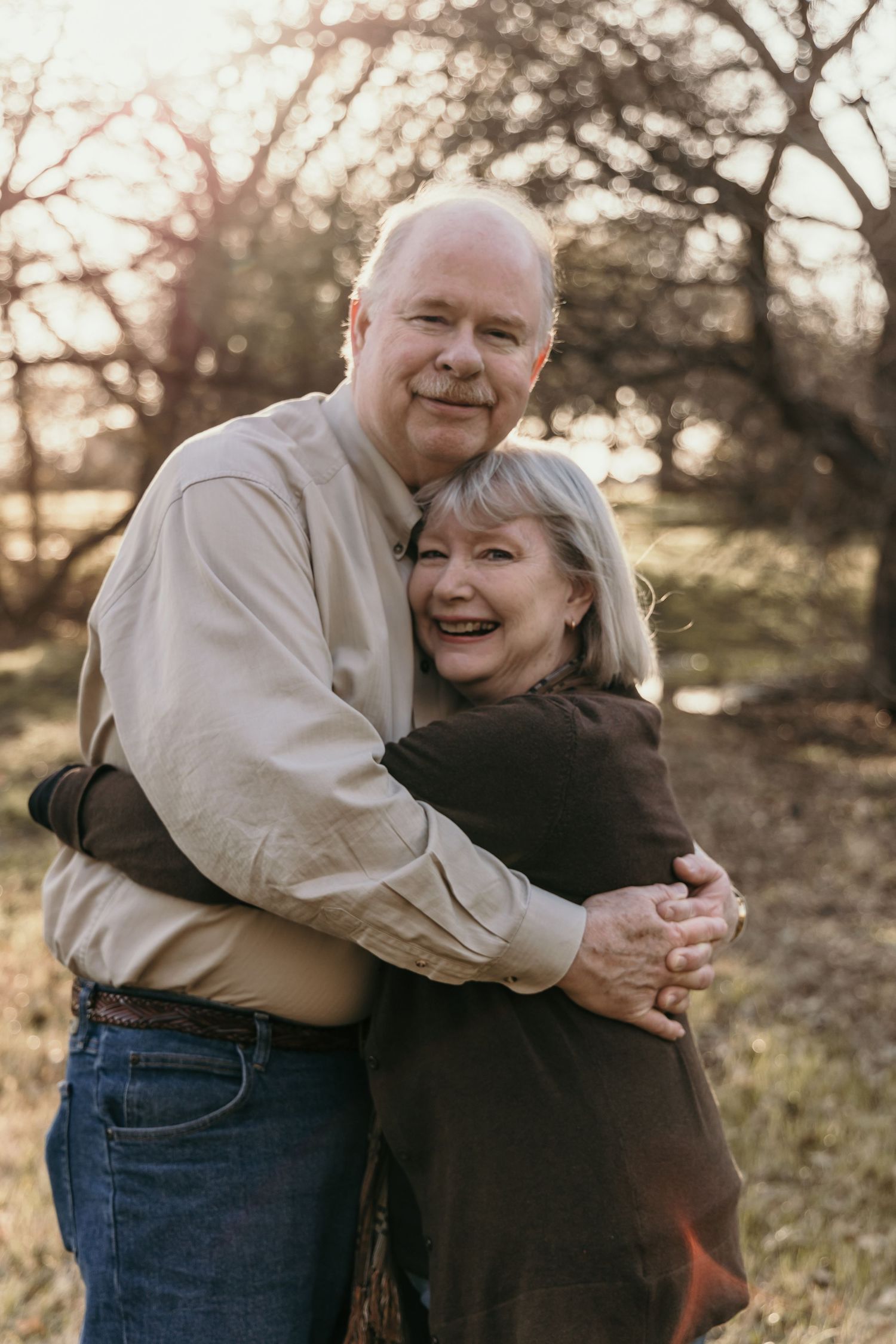 Happy older couple embracing outdoors in a park during golden hour, smiling warmly at the camera.