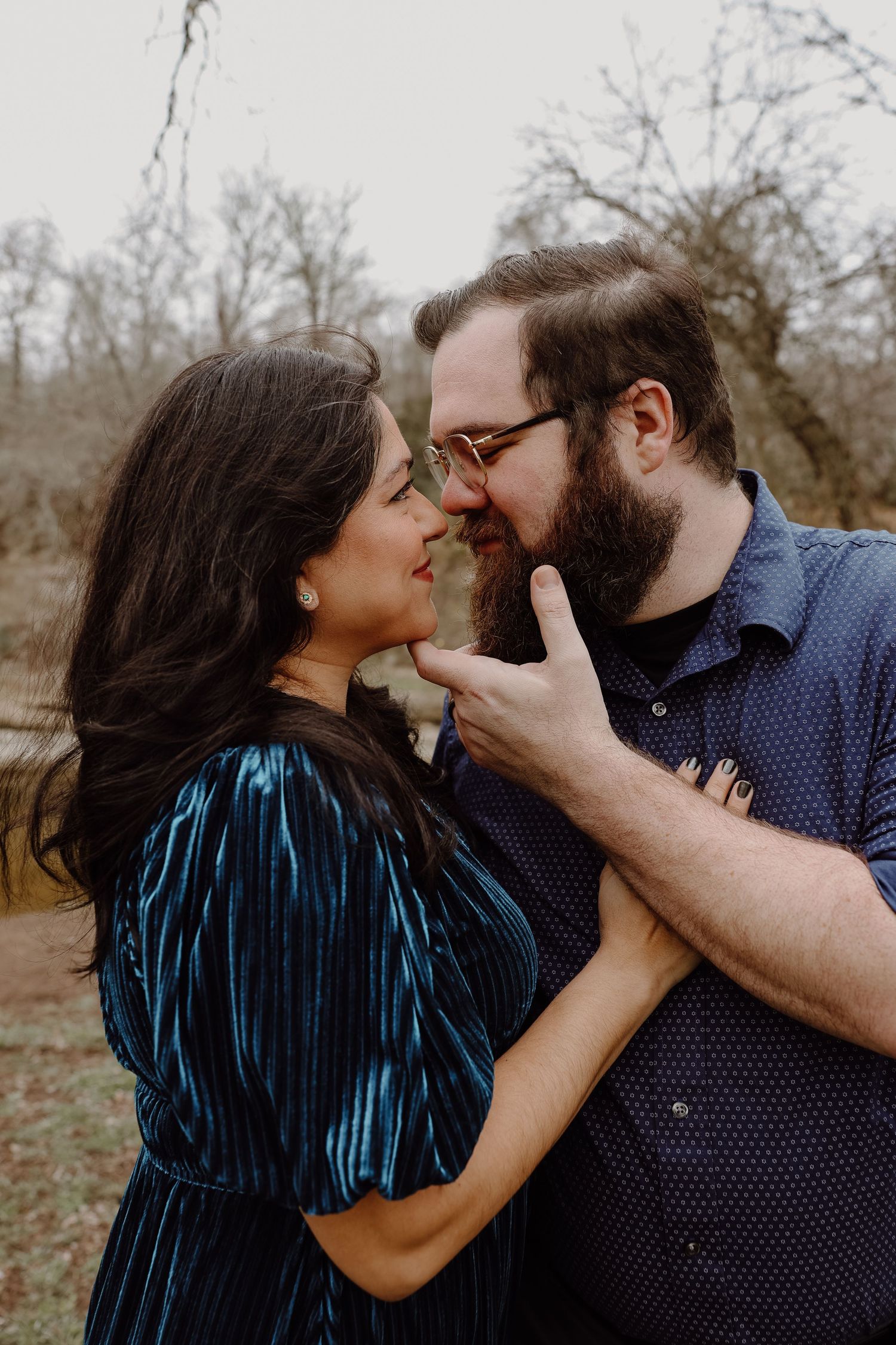 Couple sharing a tender moment, woman touching mans beard as they lean in close outdoors.