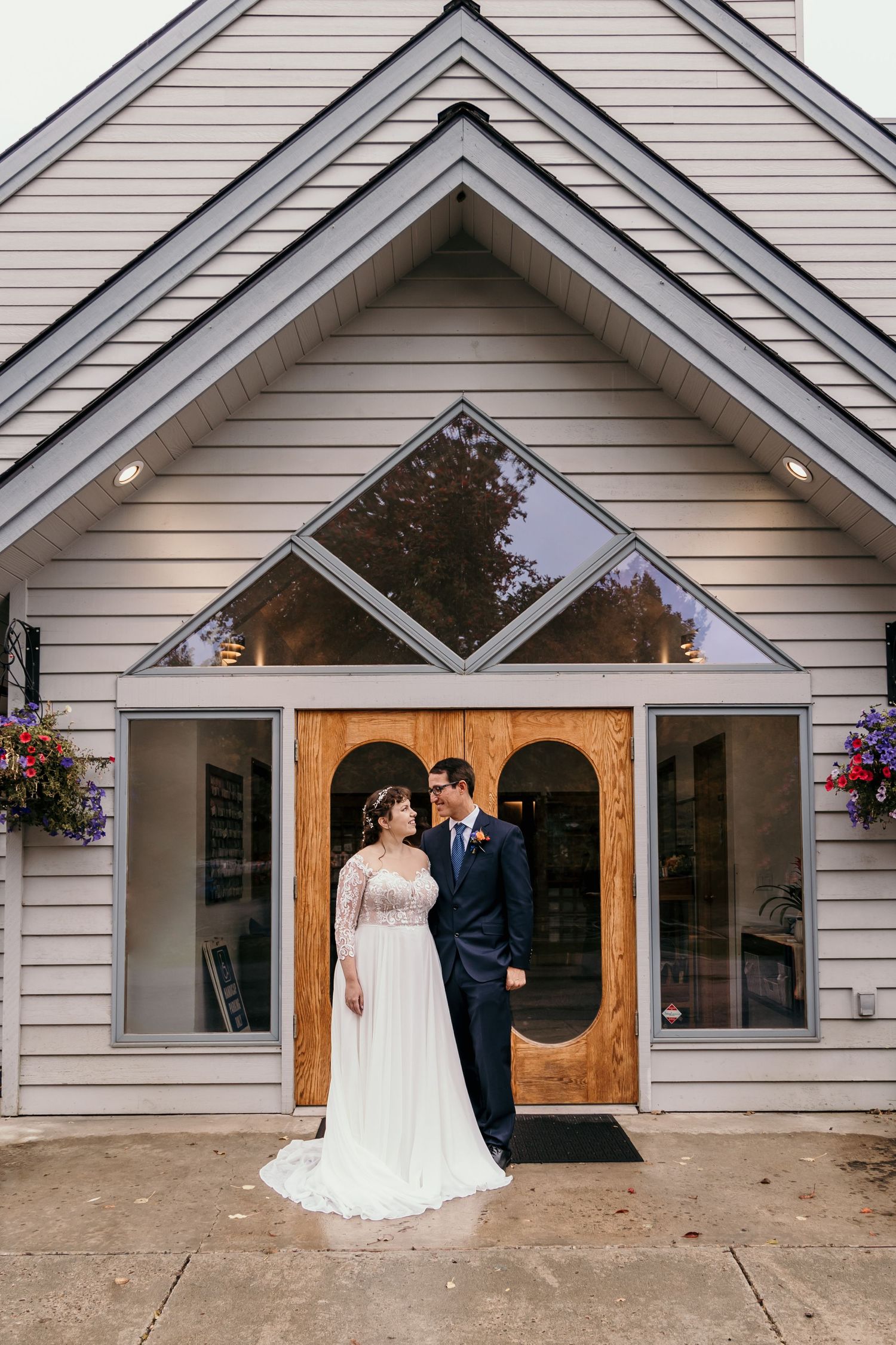 Bride and groom pose before a charming chapel with wooden doors and geometric windows on their wedding day.