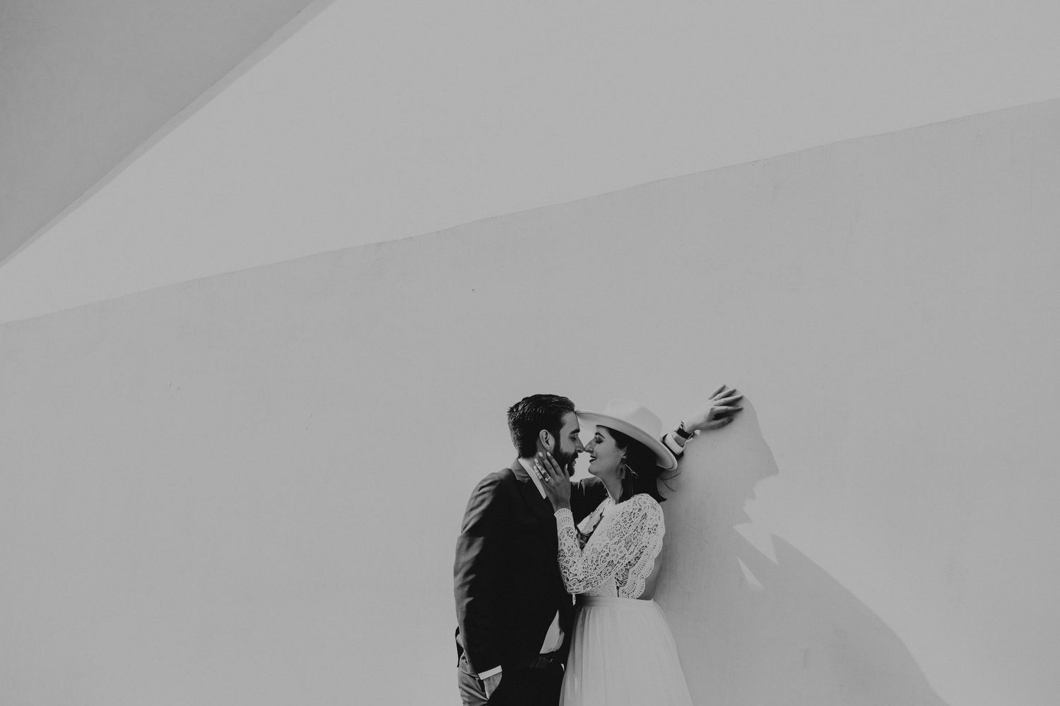 Black and white photo of a bride and groom sharing a romantic kiss against a minimalist white wall.