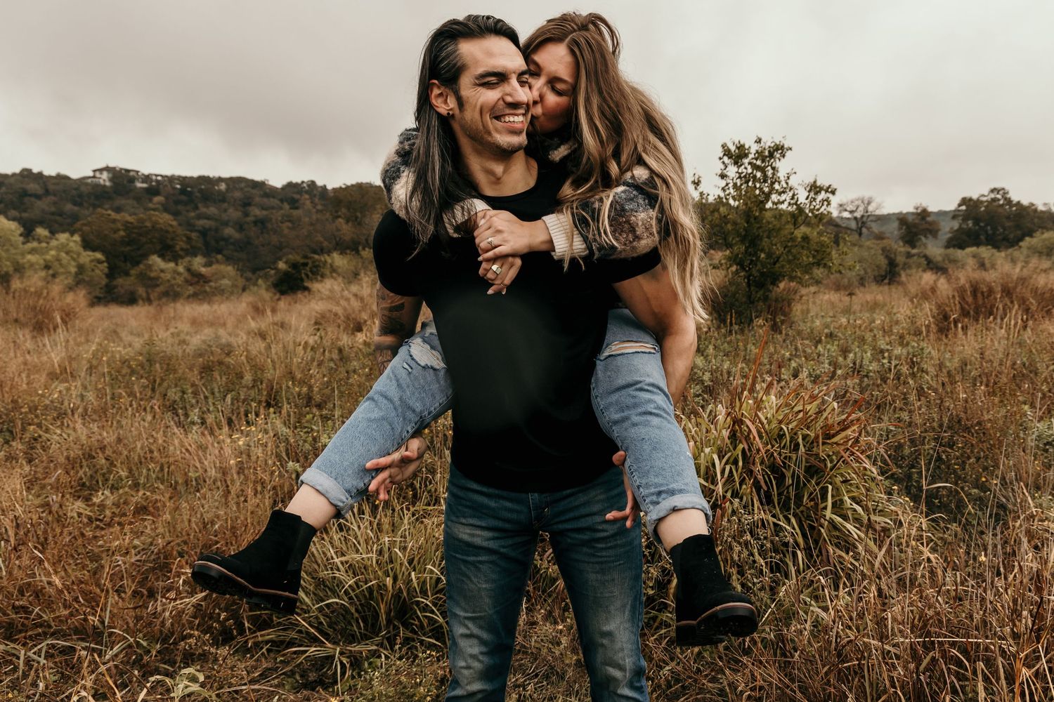Joyful couple in an autumn field, man giving woman a piggyback ride while both laugh happily.