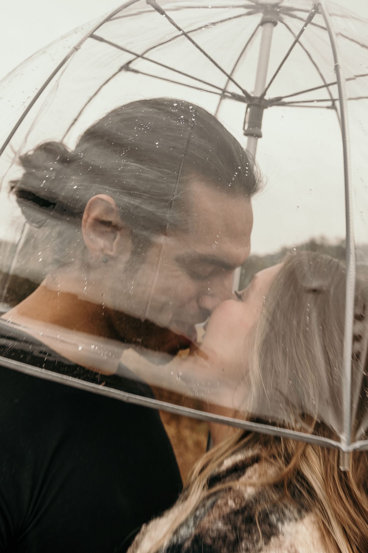 Romantic couple sharing a kiss under a clear bubble umbrella in the rain.