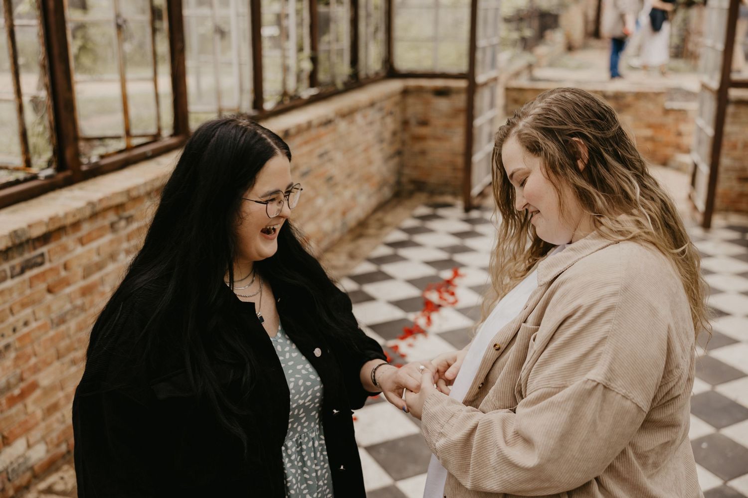 Two women sharing a joyful moment during a ring exchange in a greenhouse.