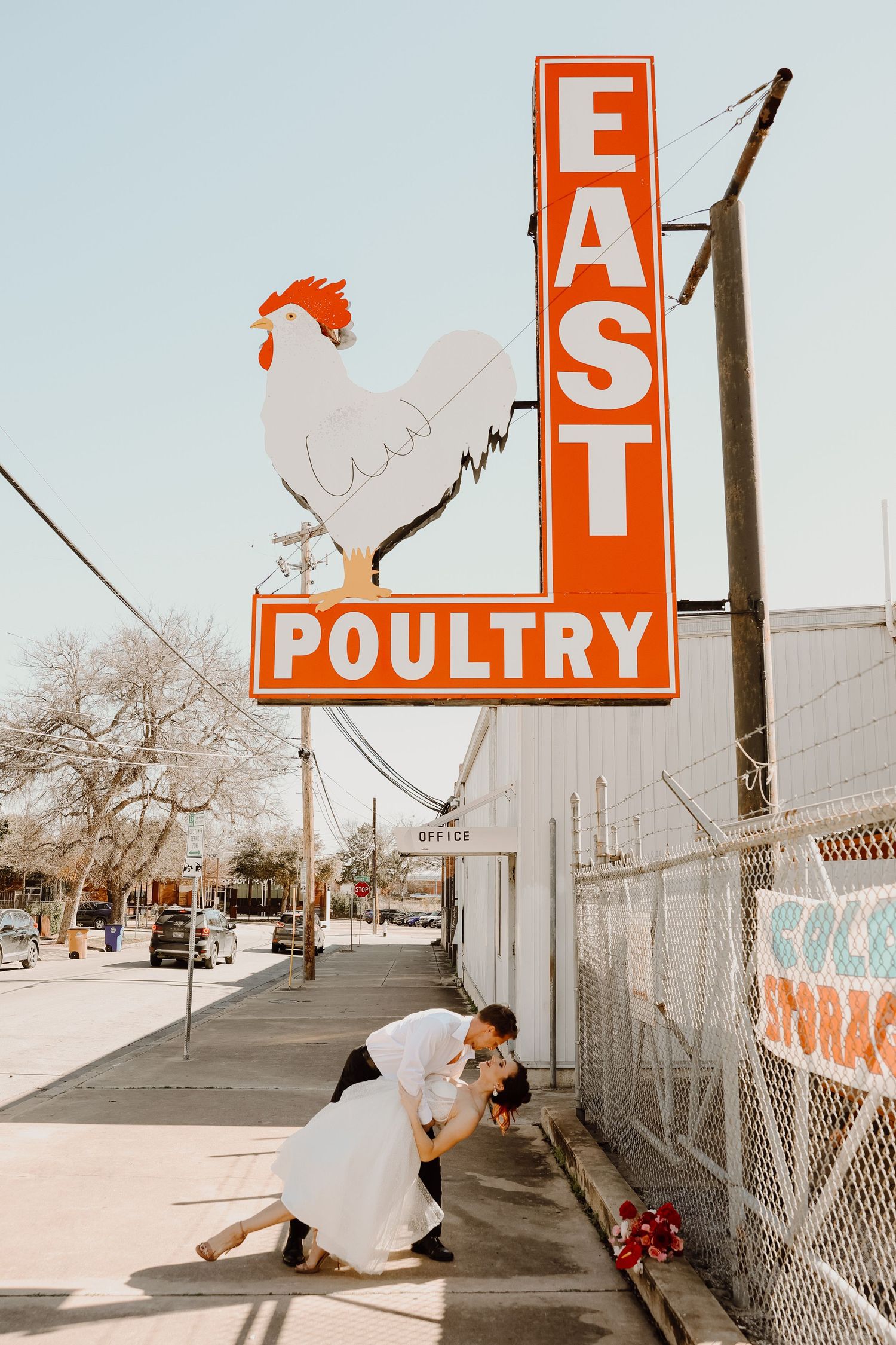 Bride and groom sharing a romantic dip kiss beneath a vintage East Poultry sign outdoors.