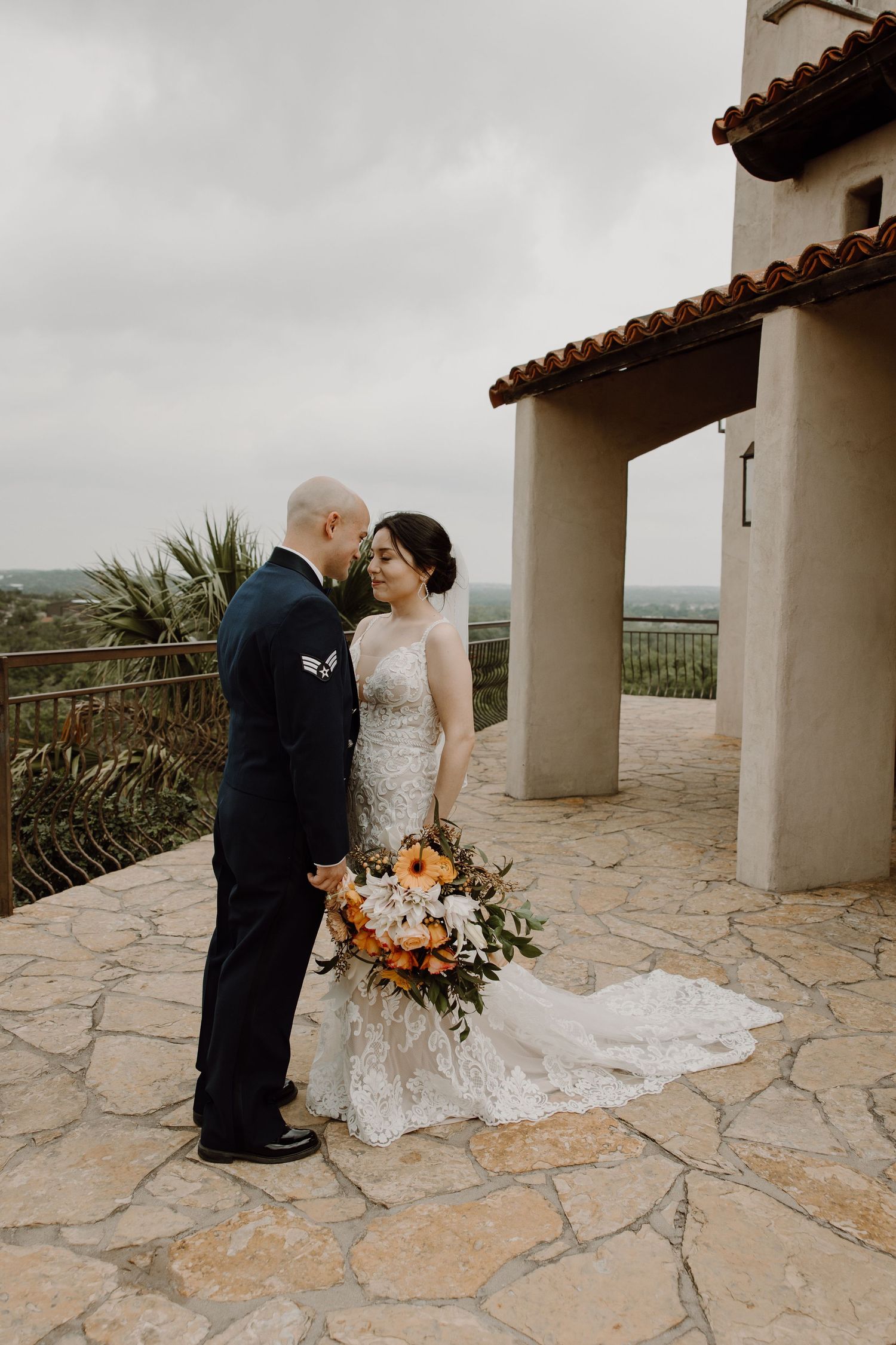 Bride and groom share an intimate moment on a stone terrace with scenic hilltop views on their wedding day.