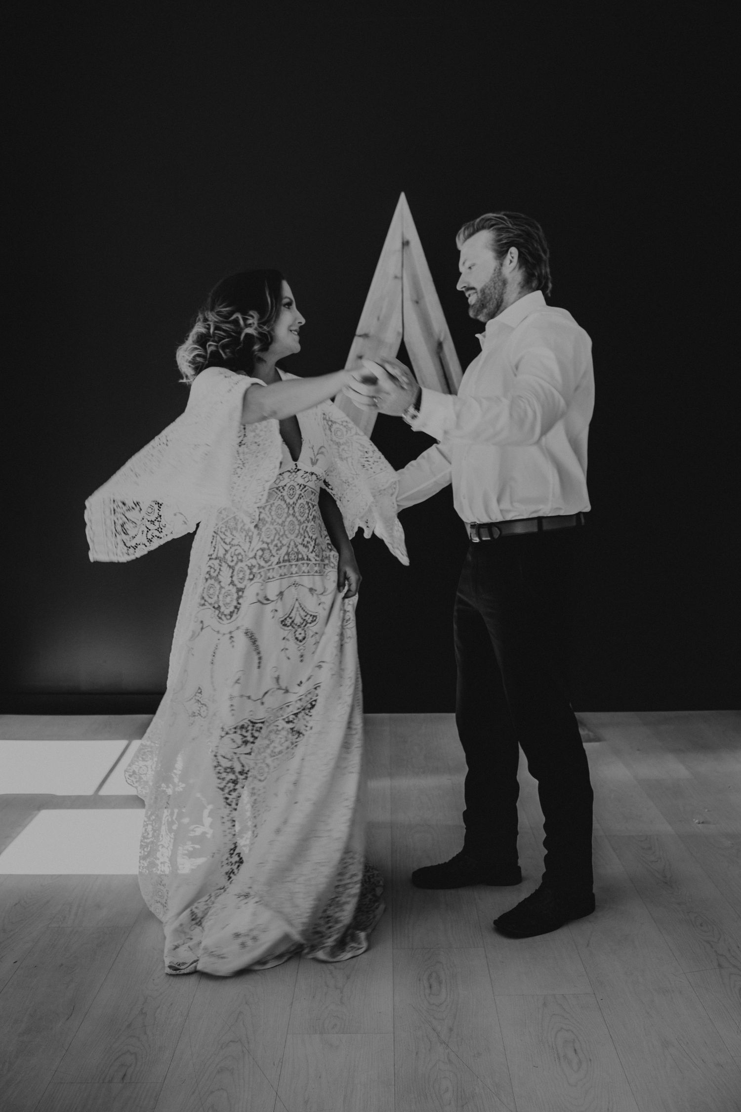 Black and white photo of a couple dancing together in wedding attire, with a geometric triangle backdrop.