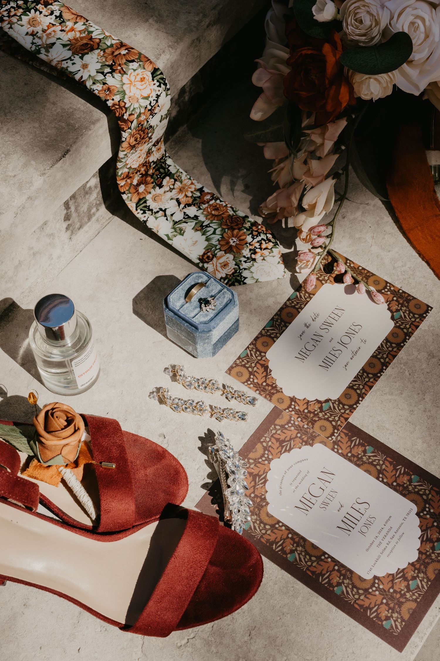 Flat lay of wedding details including red heels, invitations, jewelry, and floral accessories on stone.
