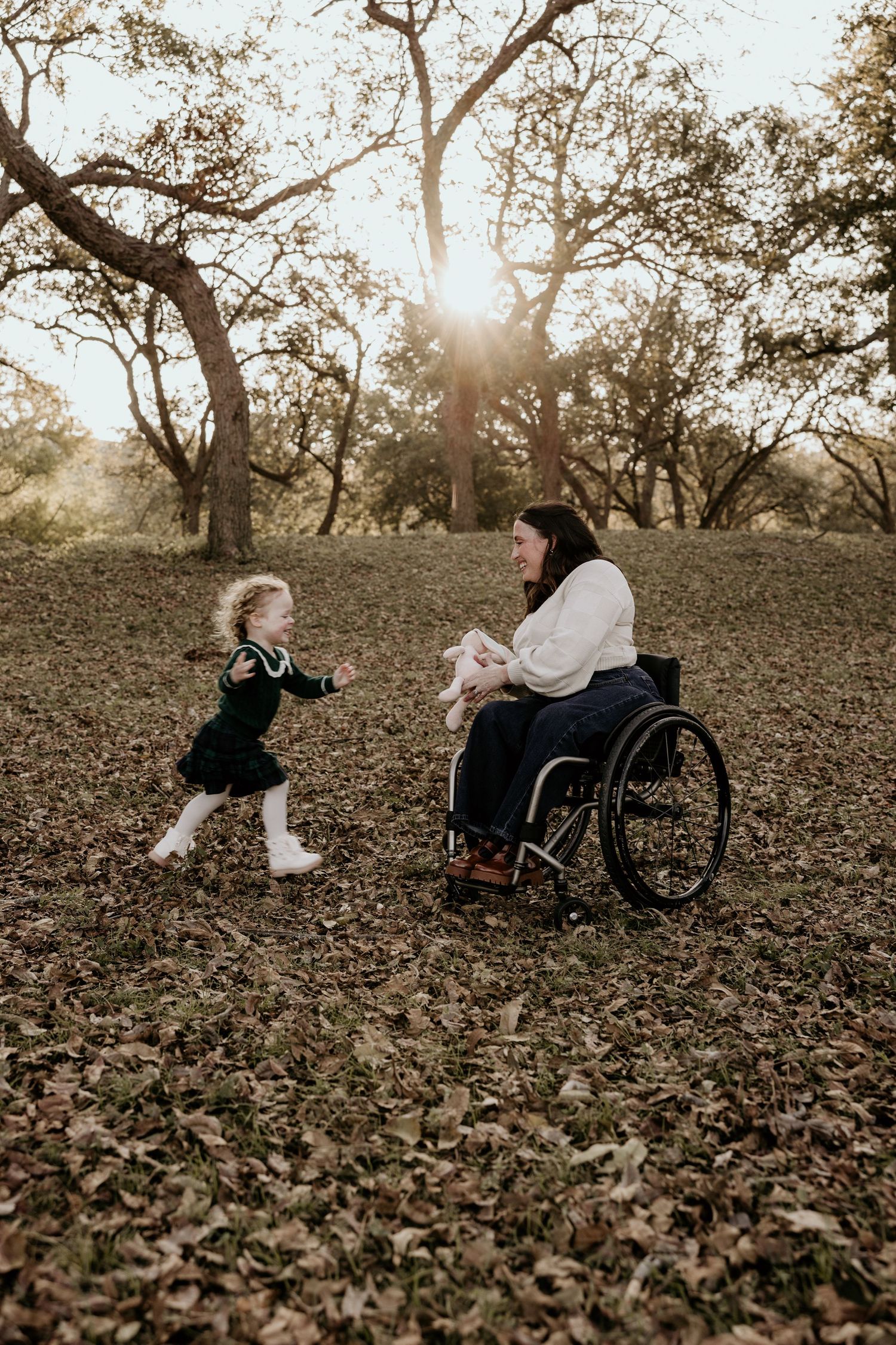 Toddler girl in green dress running toward mother in wheelchair at golden sunset in autumn park.