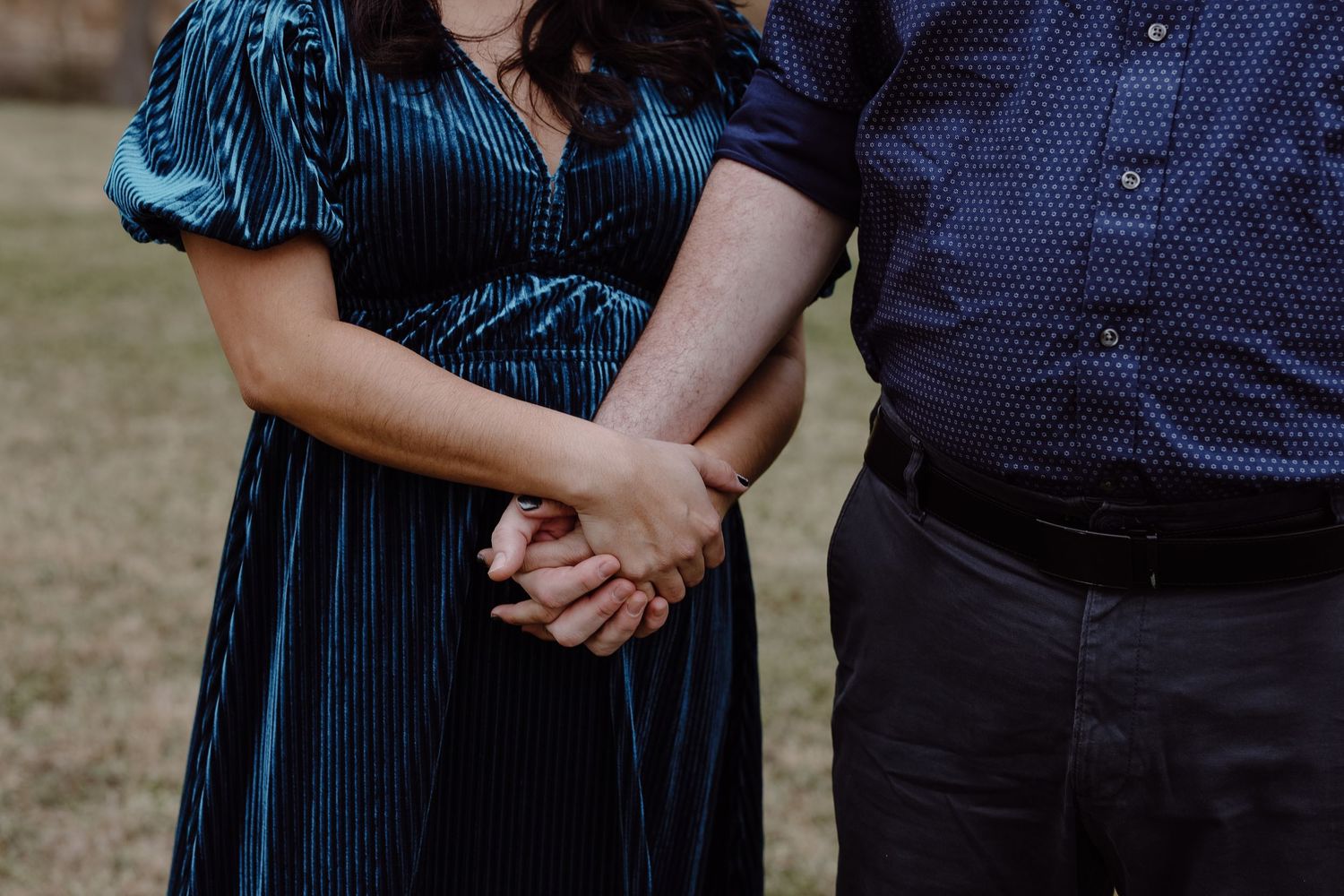 Close-up of a couple holding hands, woman wearing a teal velvet dress and man in navy shirt.