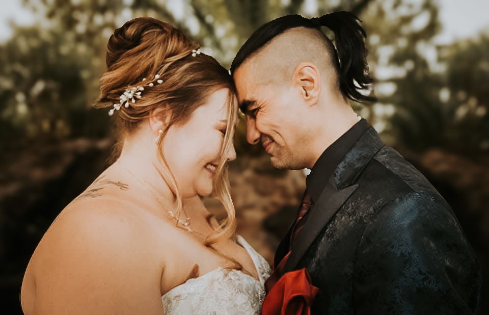 A bride and groom embrace tenderly in a romantic outdoor setting.