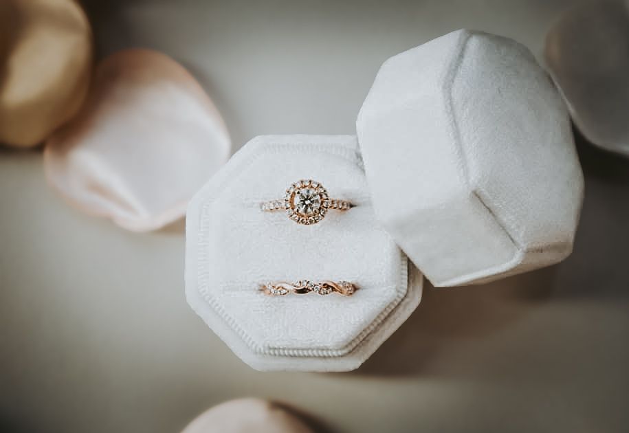 A close-up of a diamond engagement ring and wedding band in a white velvet box.