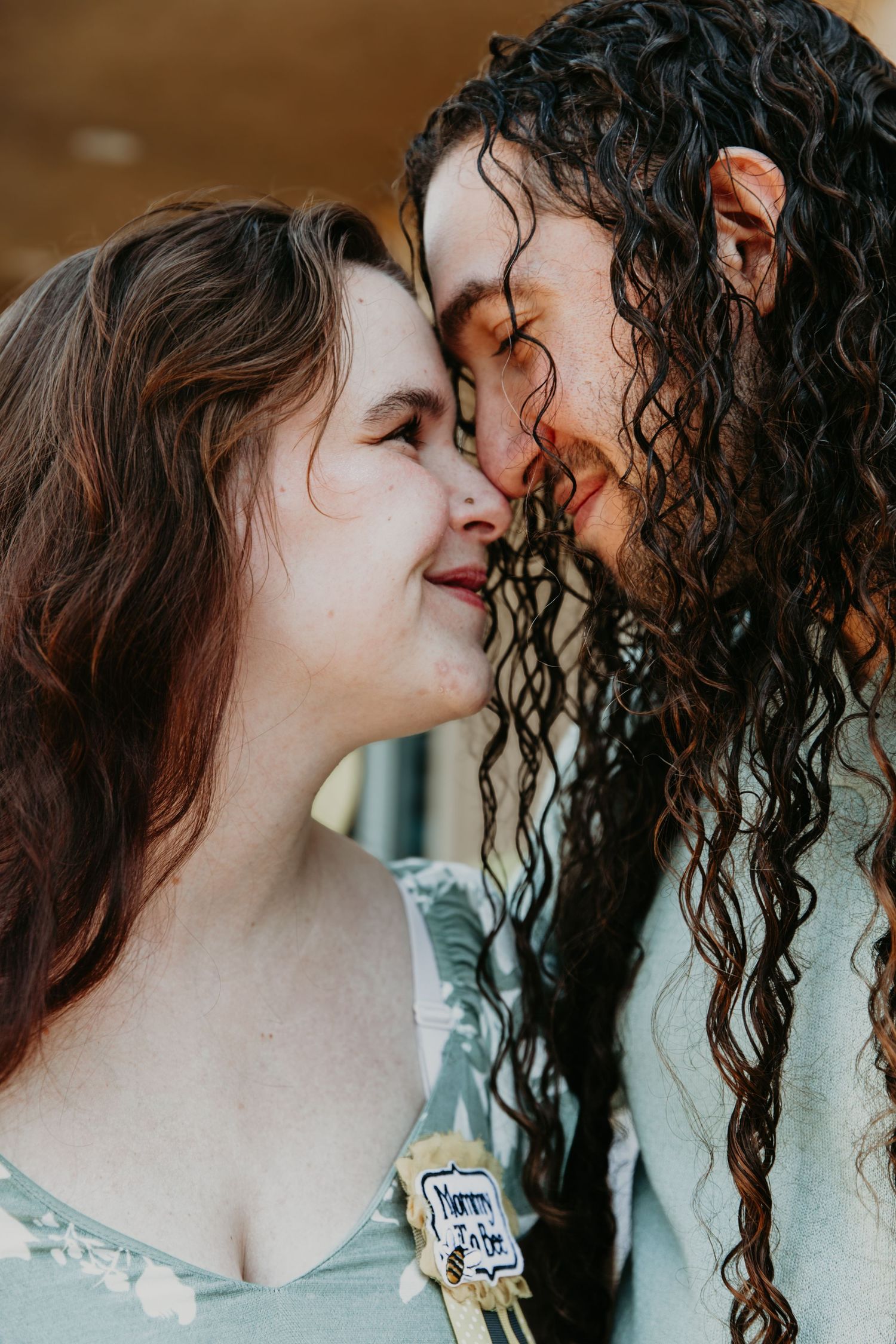 Romantic couple touching foreheads and smiling, woman with brown hair and man with curly hair sharing an intimate moment.