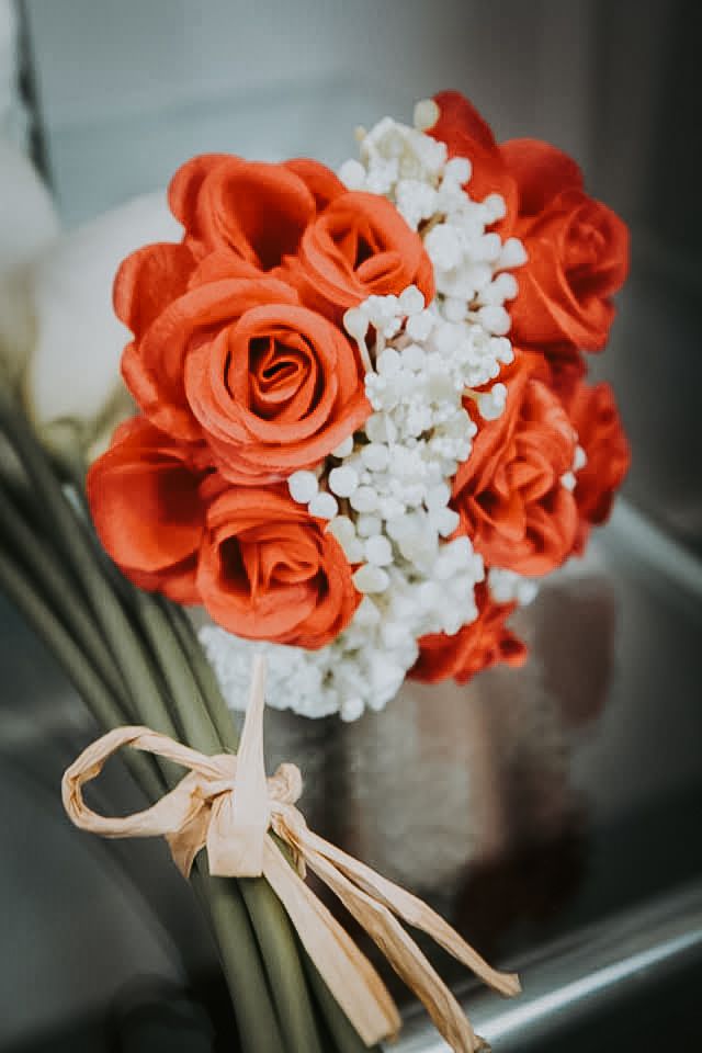 A bouquet of vibrant orange roses with white flowers, tied together with a ribbon.