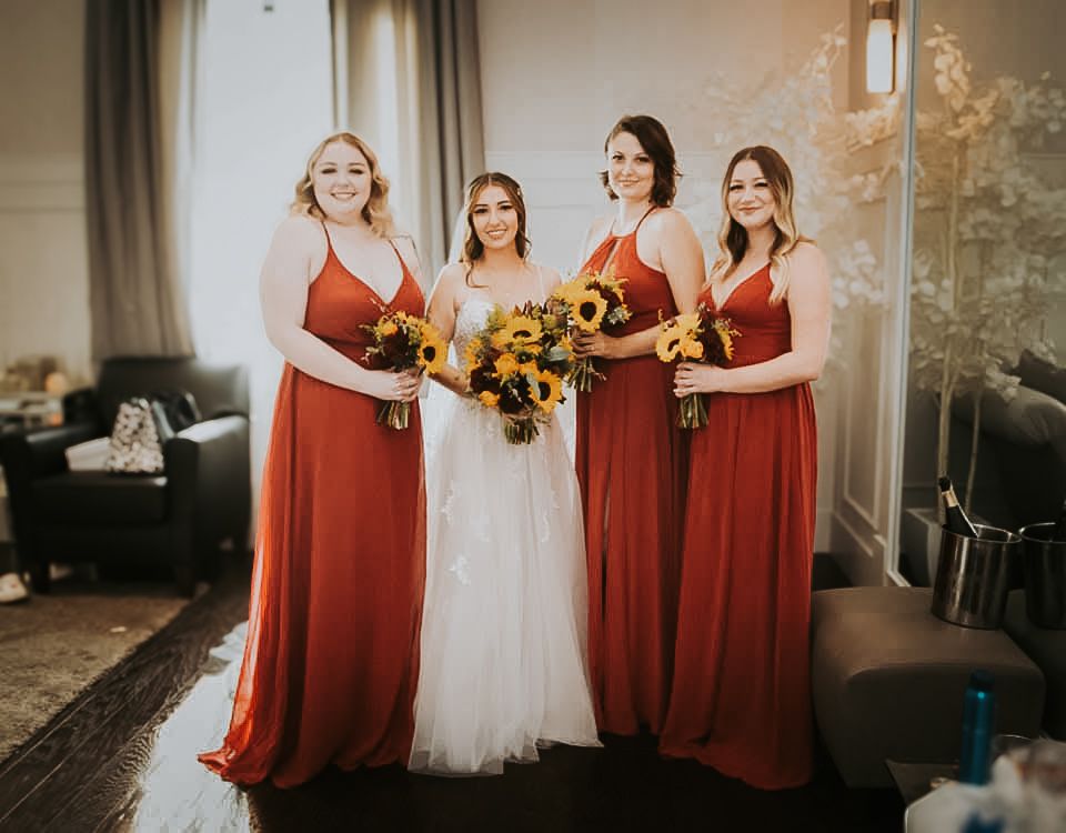 Three bridesmaids in red dresses standing next to a bride in a white wedding gown.