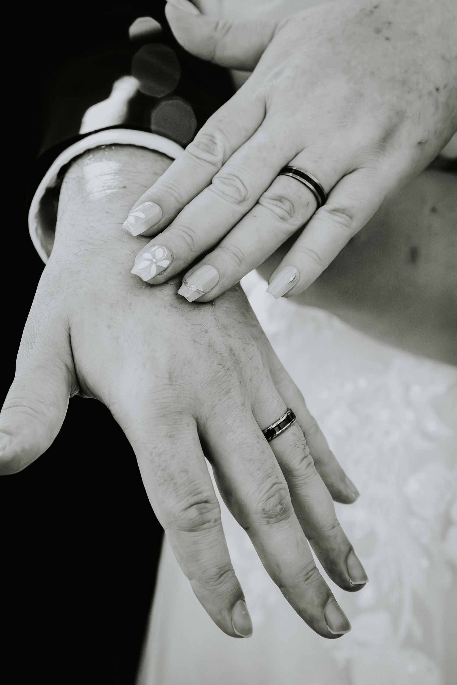 Black and white photo of newlyweds displaying their wedding rings on joined hands.