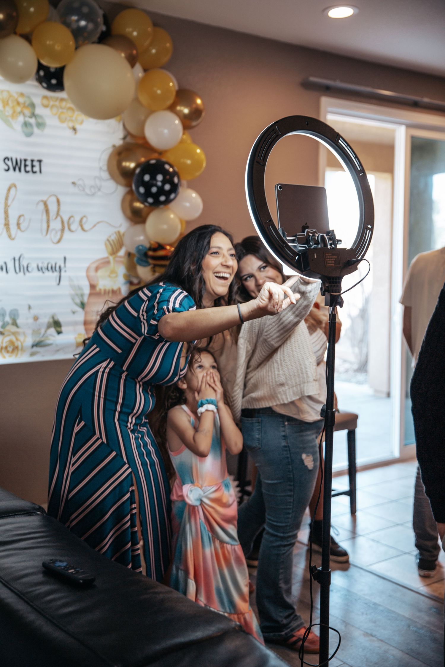 Family taking a selfie with a ring light at a baby shower with balloon decorations and a Little Bee banner.