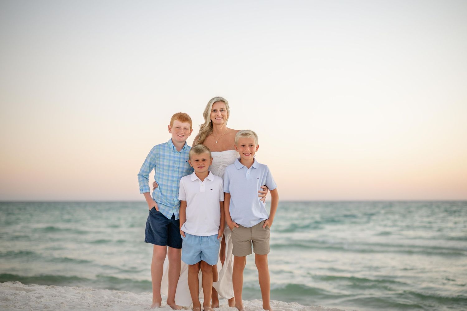 A family of four poses together on a beach during sunset with the ocean behind them.