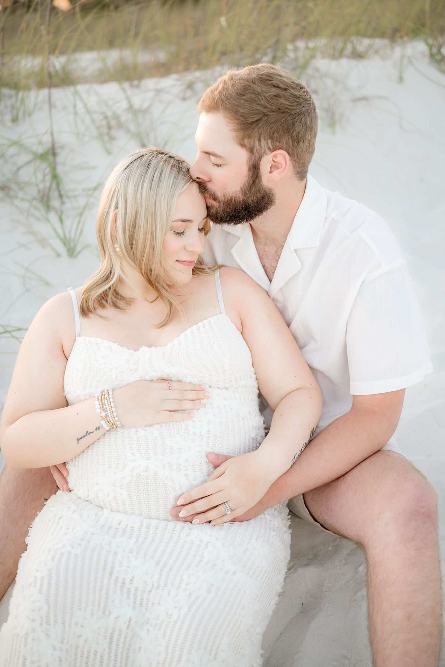 Intimate maternity photos on white sand beach with soft natural lighting.