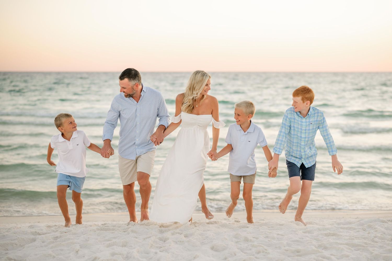 Group enjoying a playful moment while walking along the beach at dusk with ocean waves behind them.