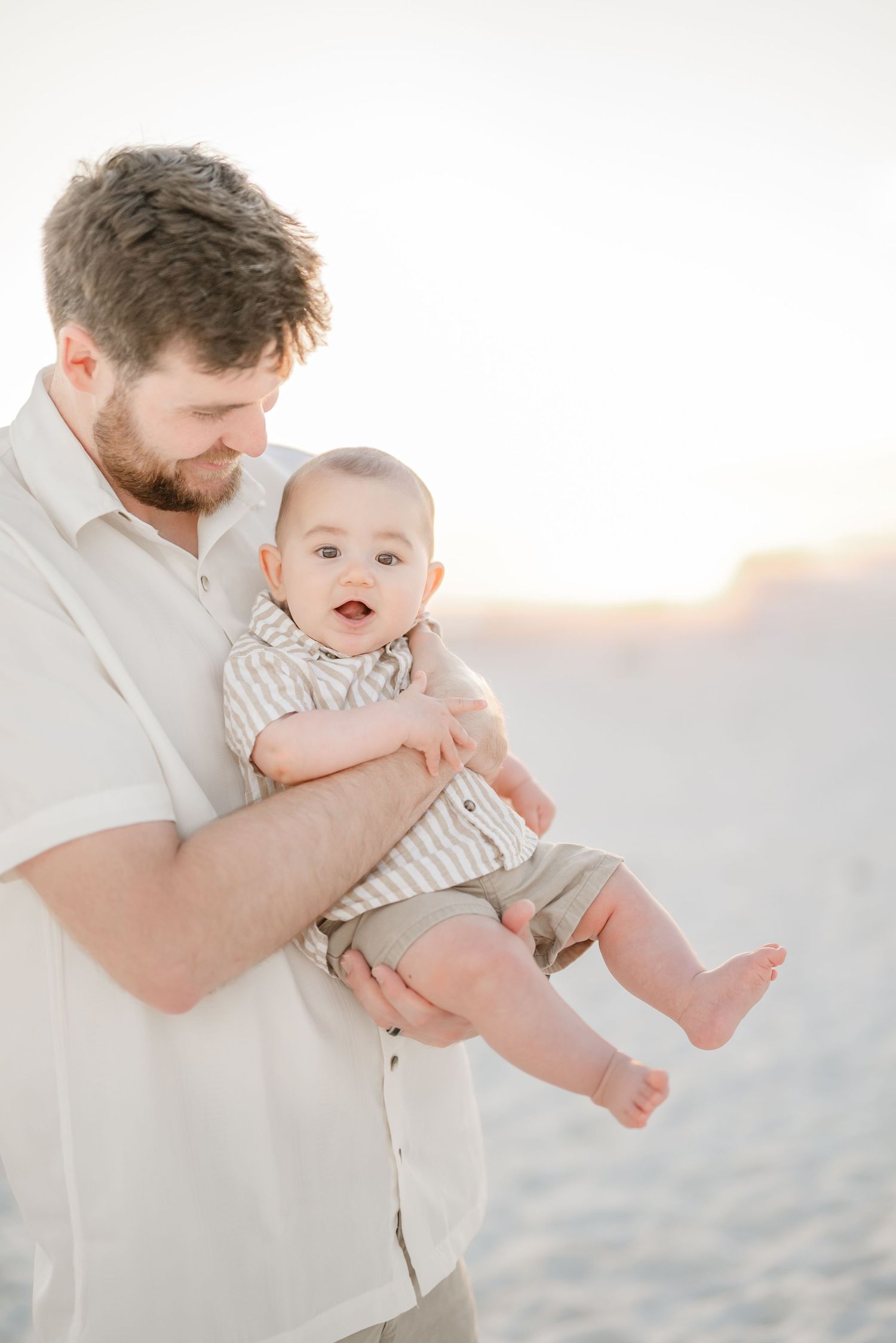 A joyful family moment playing together on a sunlit beach in white clothing.