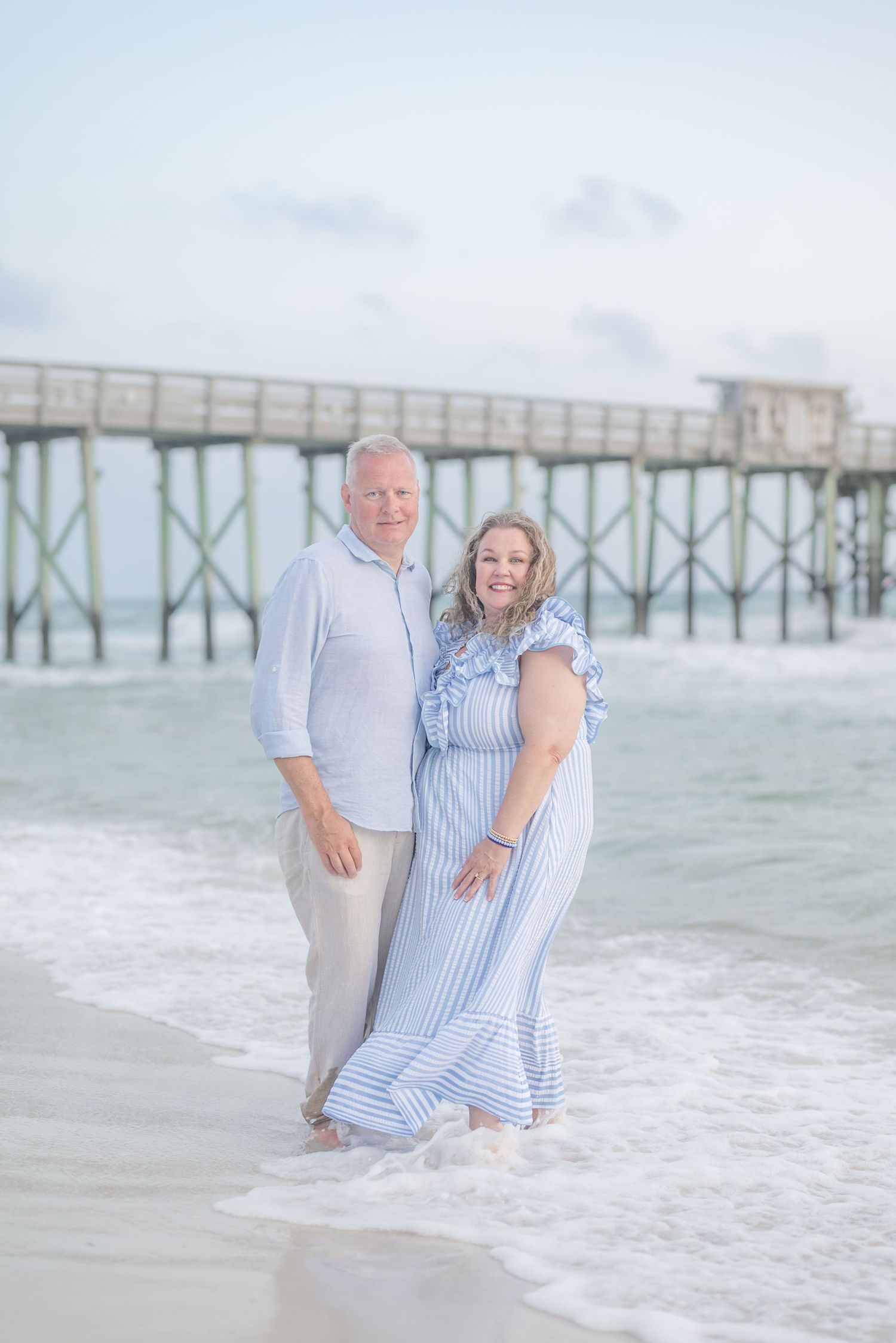 A couple stands together on a sandy beach wearing coordinating blue and white outfits.