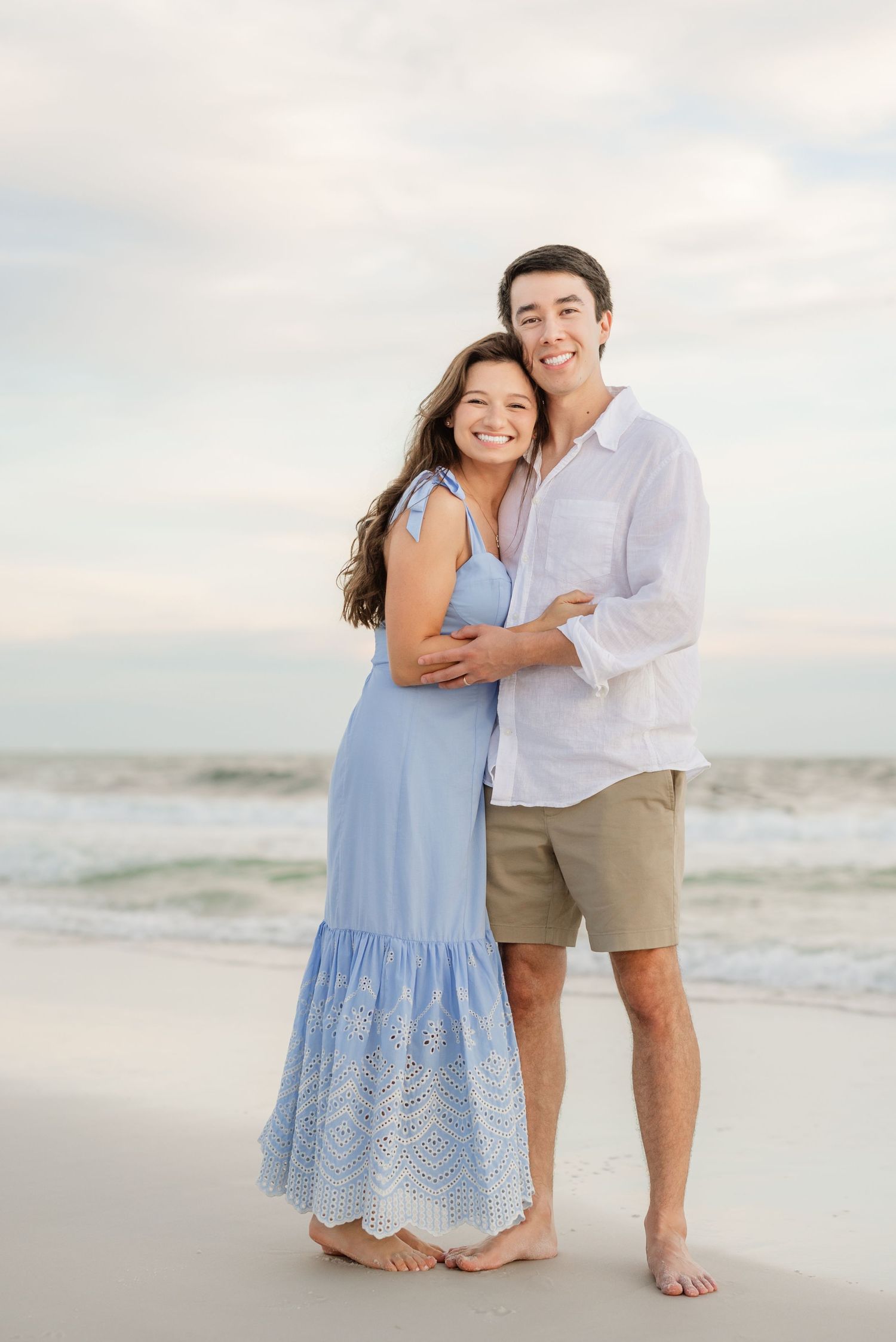 A couple shares joyful moments on the beach wearing coordinated blue and white casual attire.