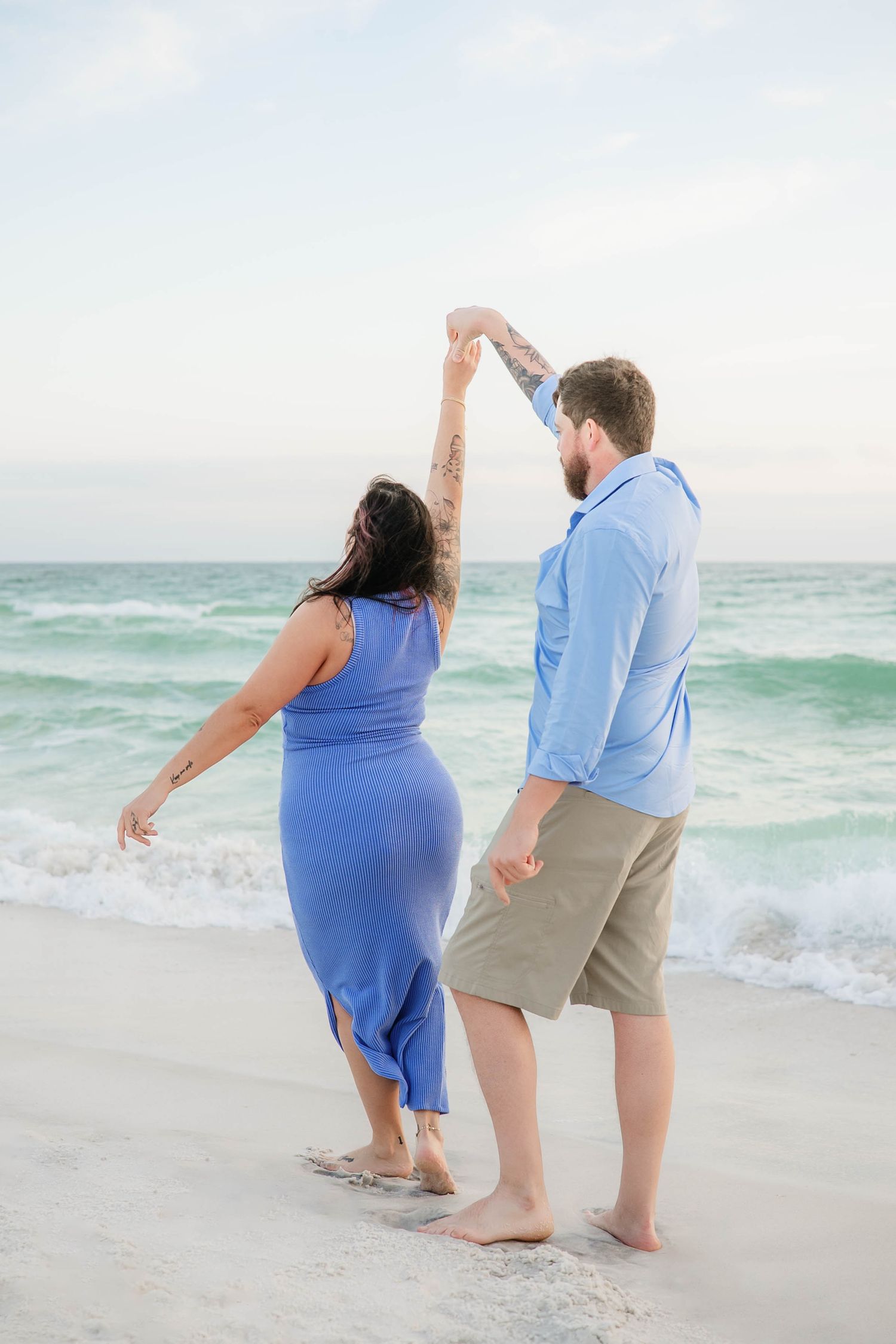 A couple playing and dancing together on a sunny beach with turquoise waters.