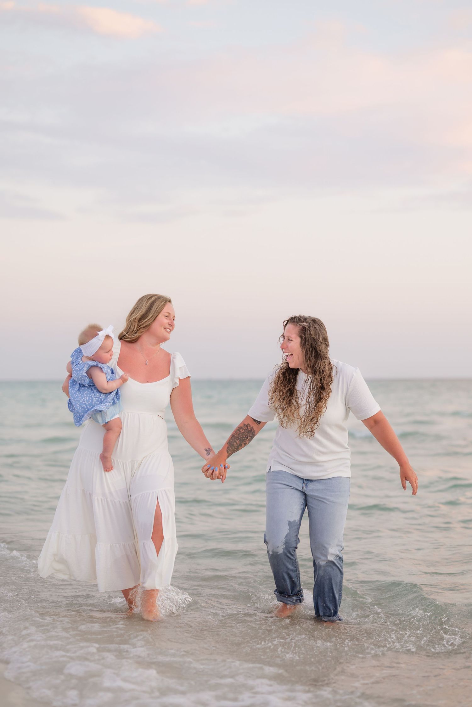Three people wade in ocean waves during a sunset beach photoshoot.