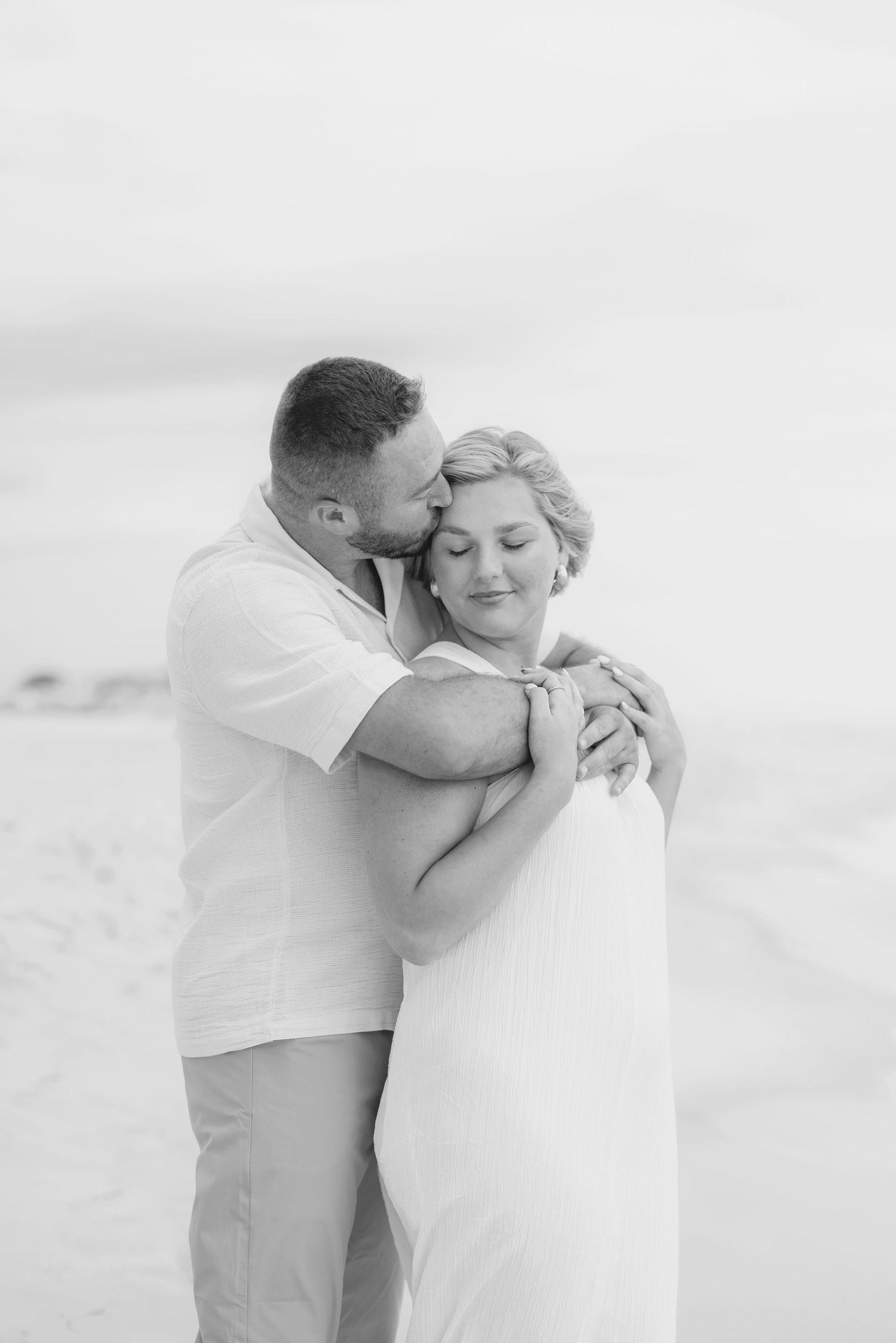 Intimate black and white portrait of couple embracing on beach.