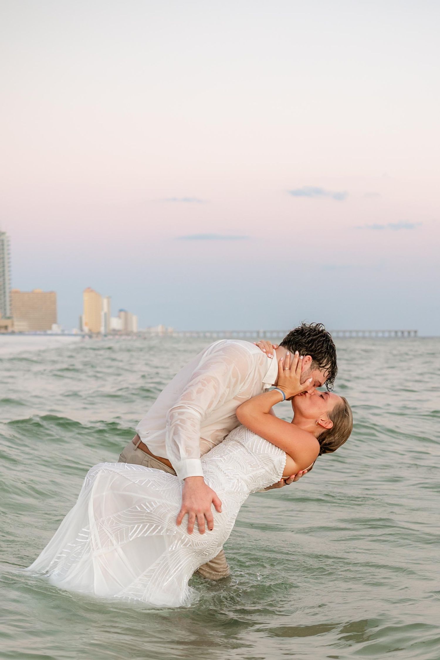 Couple in formal attire shares dramatic dip pose in ocean waters.