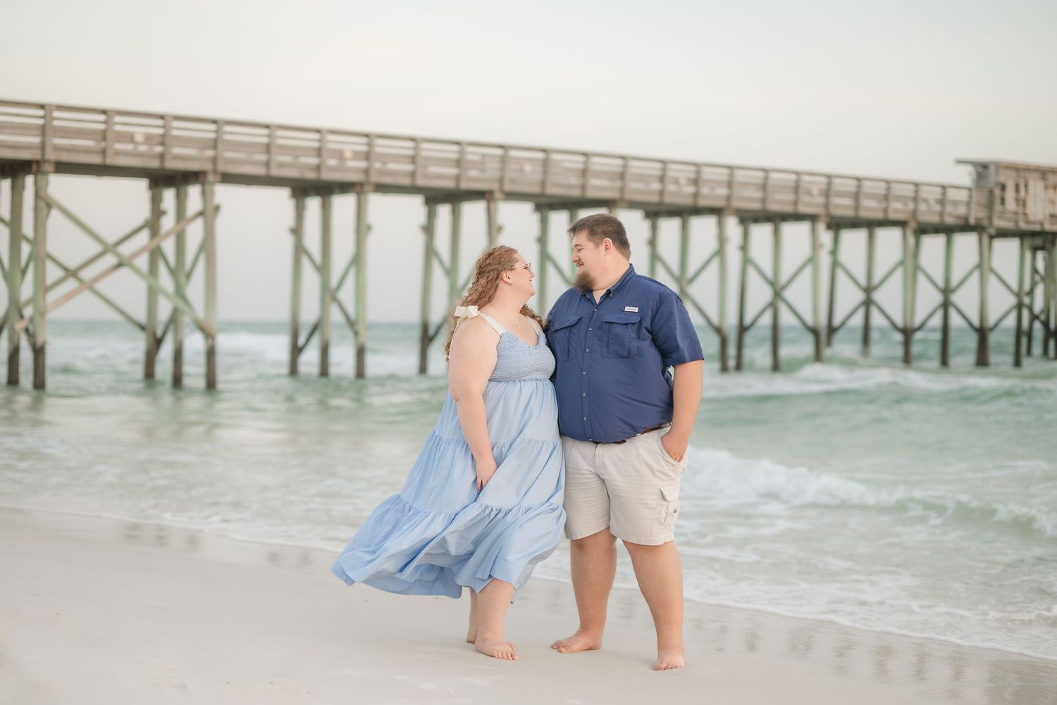 Beachside portraits near wooden pier with waves rolling in background.