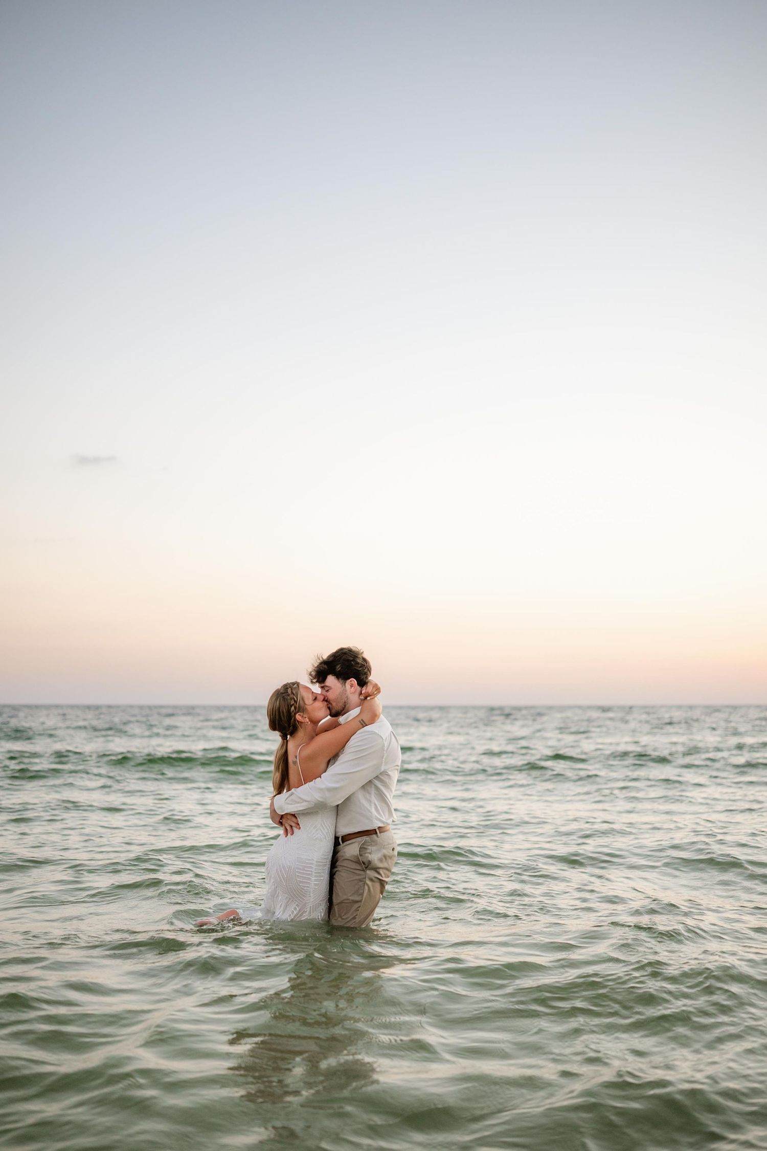 Intimate beach photography captures couple's tender moment in ocean waters.