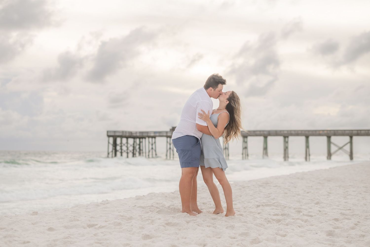Couple playing and laughing together on sandy beach near ocean pier.