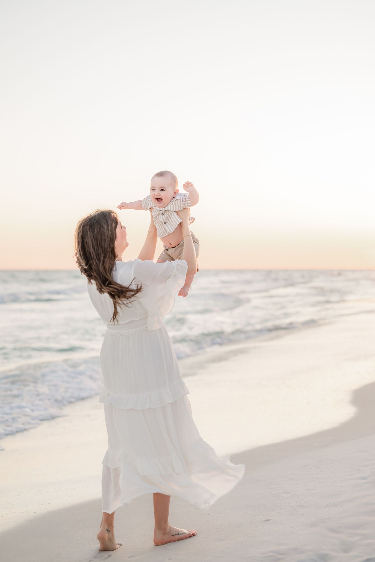 Mother and baby playing together on a white sandy beach at dusk.