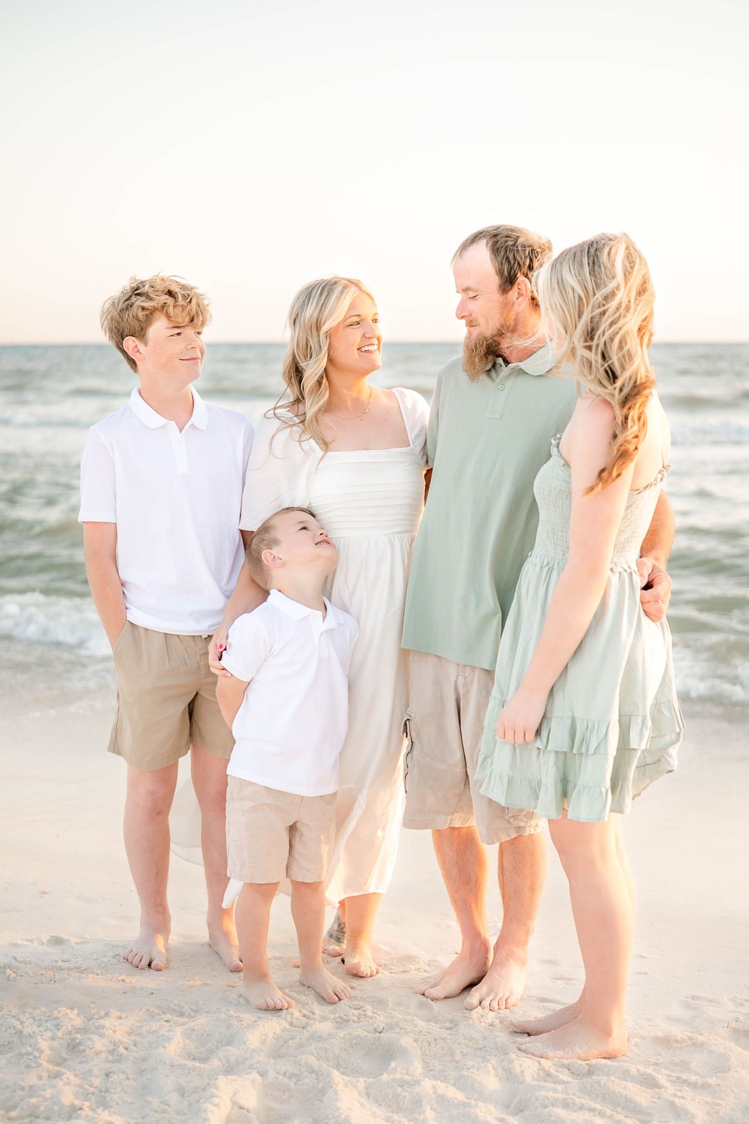 Family members' bare feet lined up together on a sandy beach at sunset.