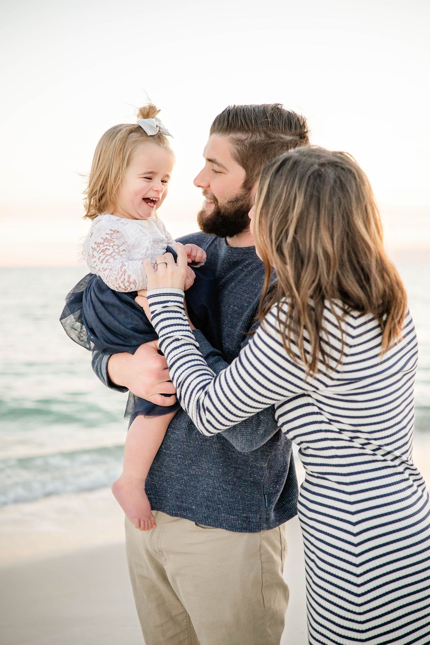 Family sharing intimate moments together on beach wearing coordinated navy and striped outfits.