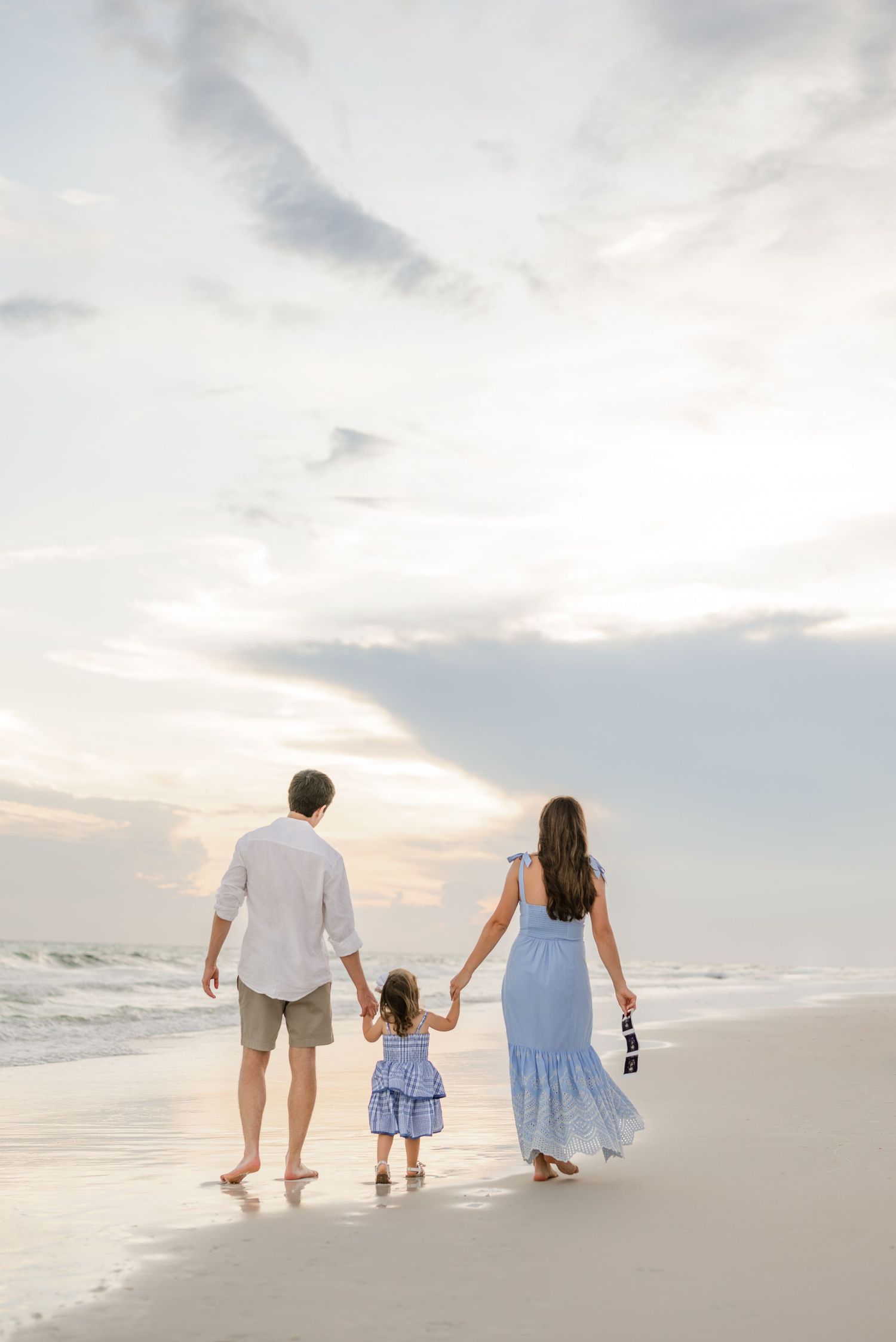 Family walking together on white sandy beach during sunset with ocean waves in background.