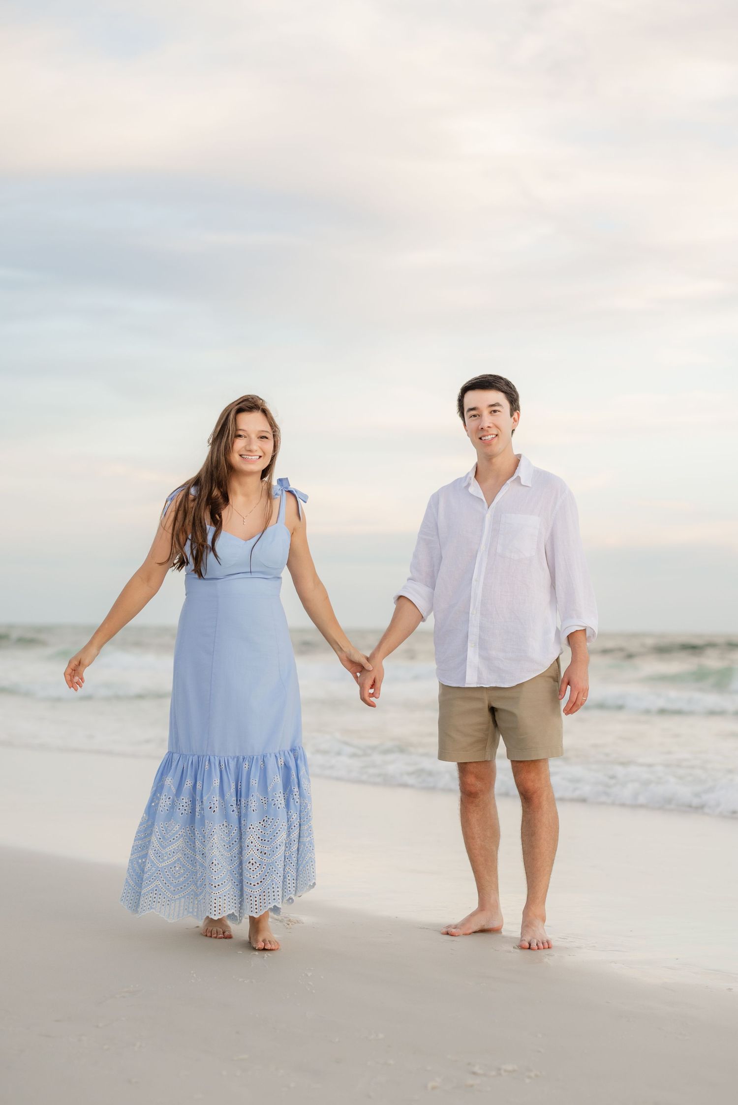 A couple walks hand in hand along the beach wearing coordinated casual outfits.