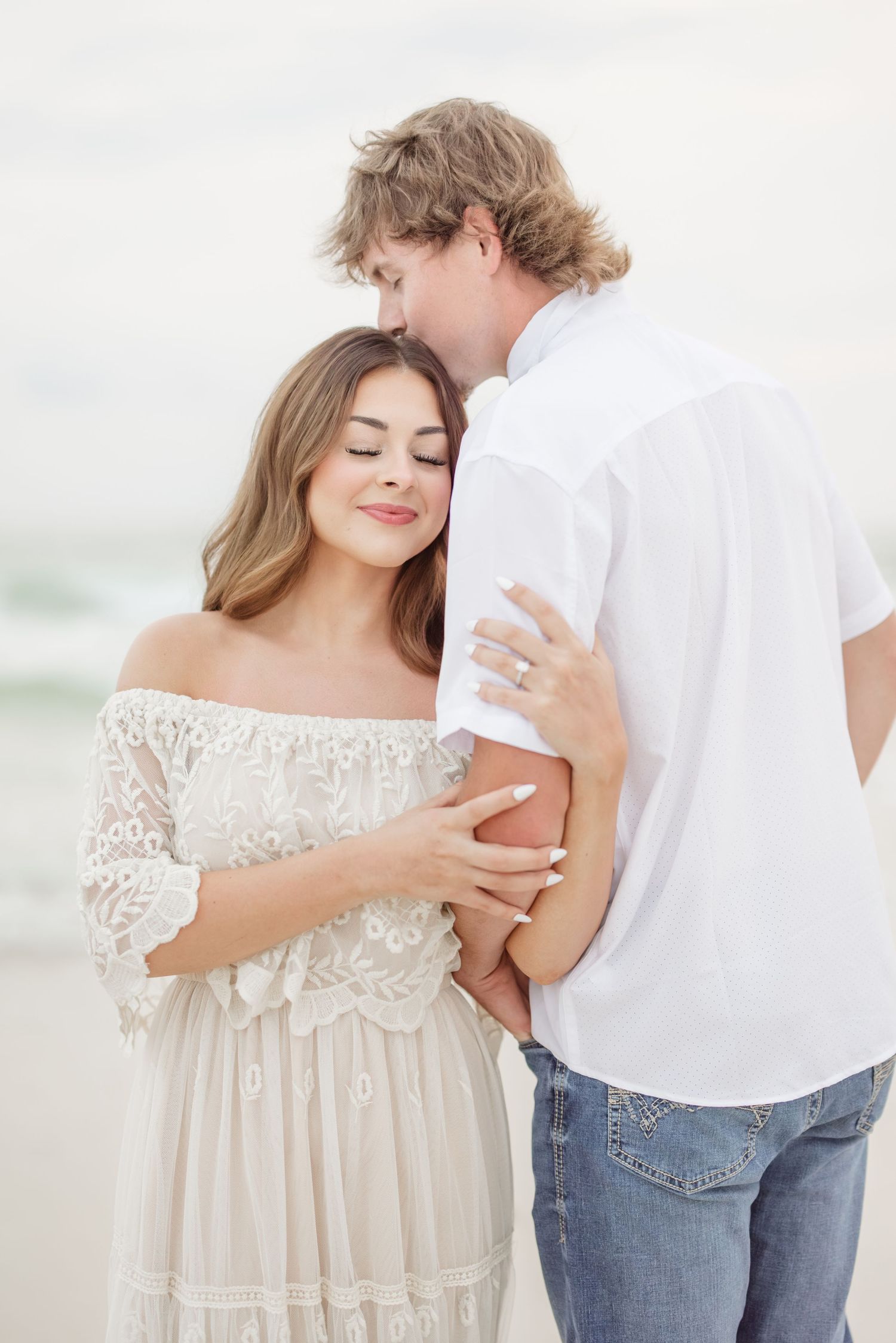 Dreamy beach portraits featuring a couple in white lace dress and casual attire.