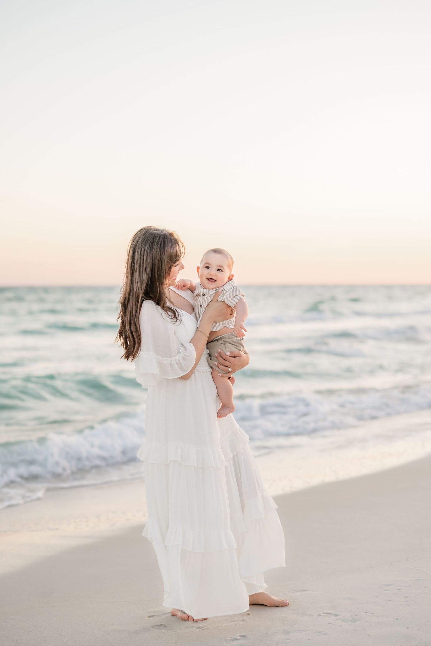 Family dressed in white enjoying playful moments on a beach at sunset.