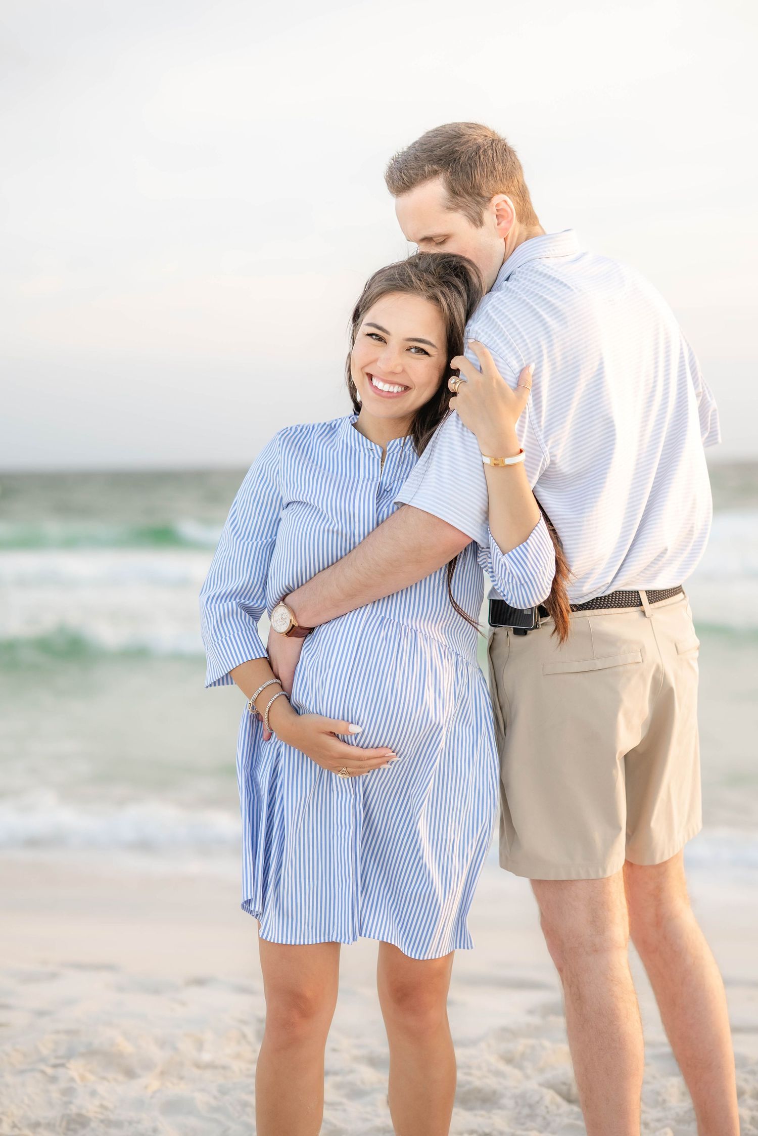A couple embraces during their maternity photo session on a sandy beach.