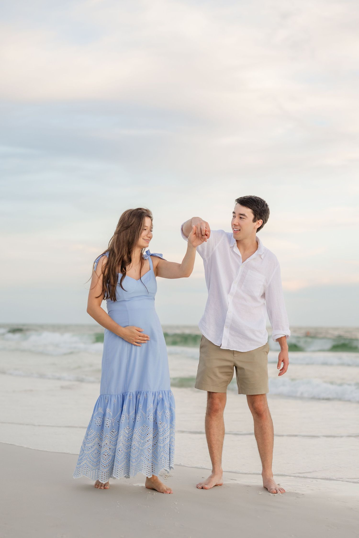 A playful couple interacts on the shoreline wearing summer beach attire.