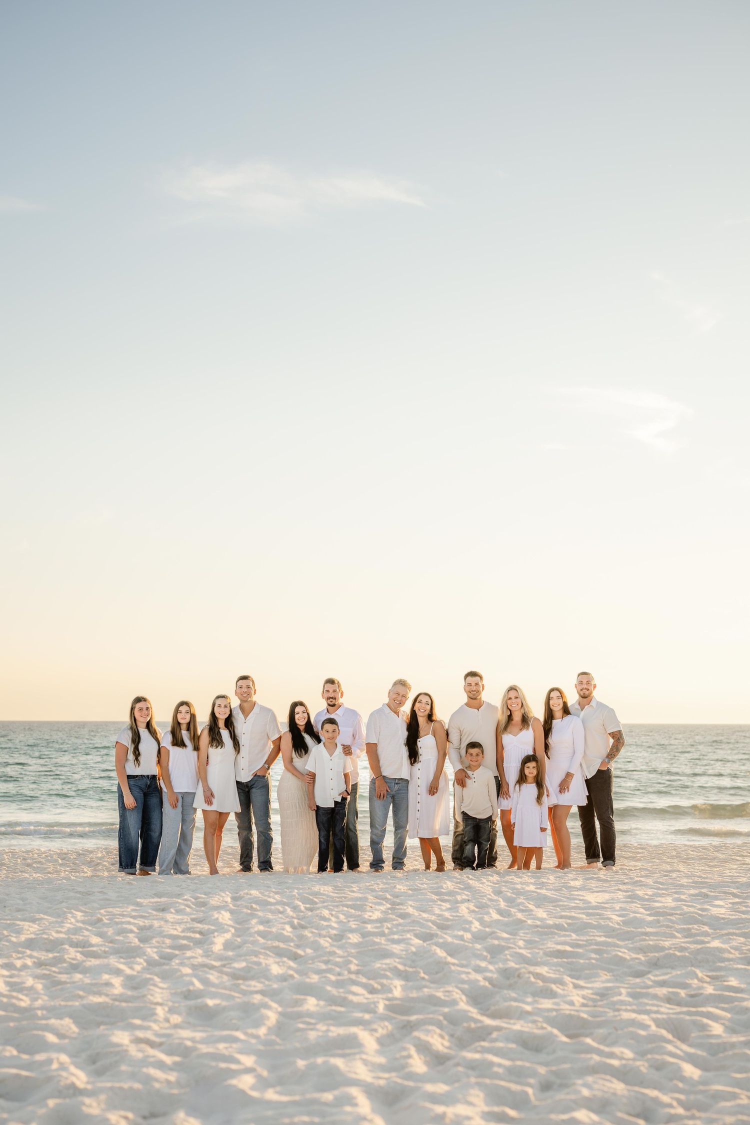 Multi-generational family group portrait on white sandy beach with ocean backdrop.